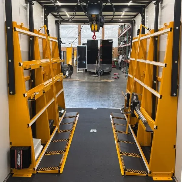 Yellow automated vehicle inspection or maintenance lift inside a garage, with black platforms and tools, and a view of the garage interior in the background.