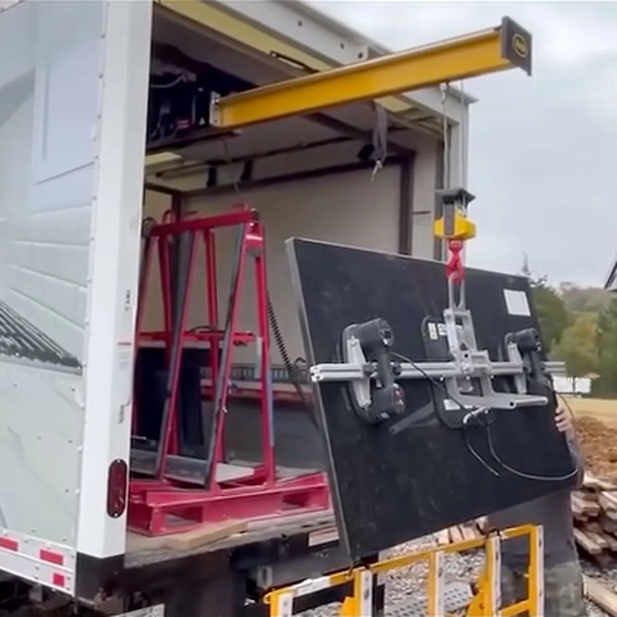 Open truck with equipment inside, including a red ladder, a black assembly with motors and sensors, and a yellow overhead crane or hoist.