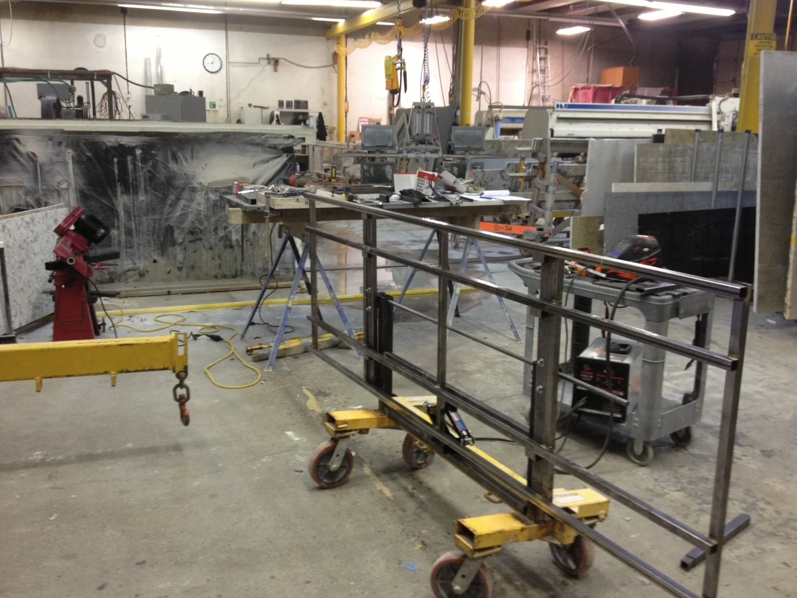 An industrial workshop with various tools, workbenches, and equipment for manufacturing or fabrication, including metal frames, cutting machines, and measuring tools.