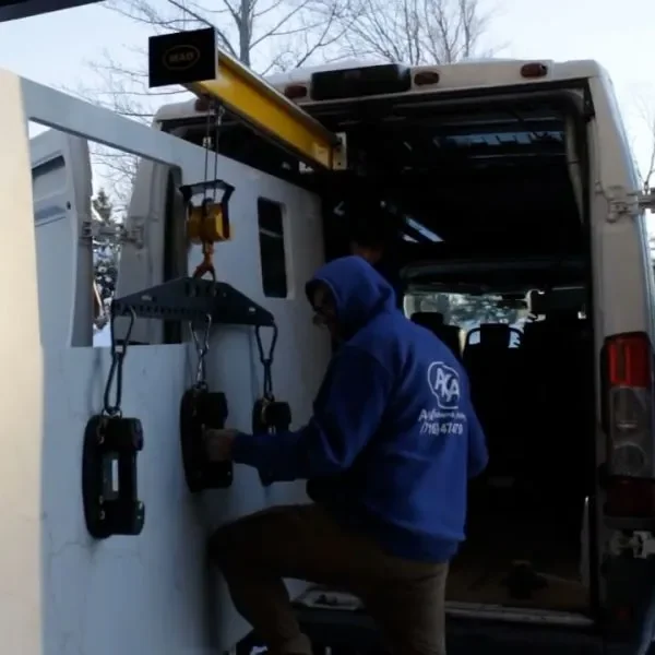 Technician in a blue hoodie working on electrical equipment mounted on a white panel inside a service van.