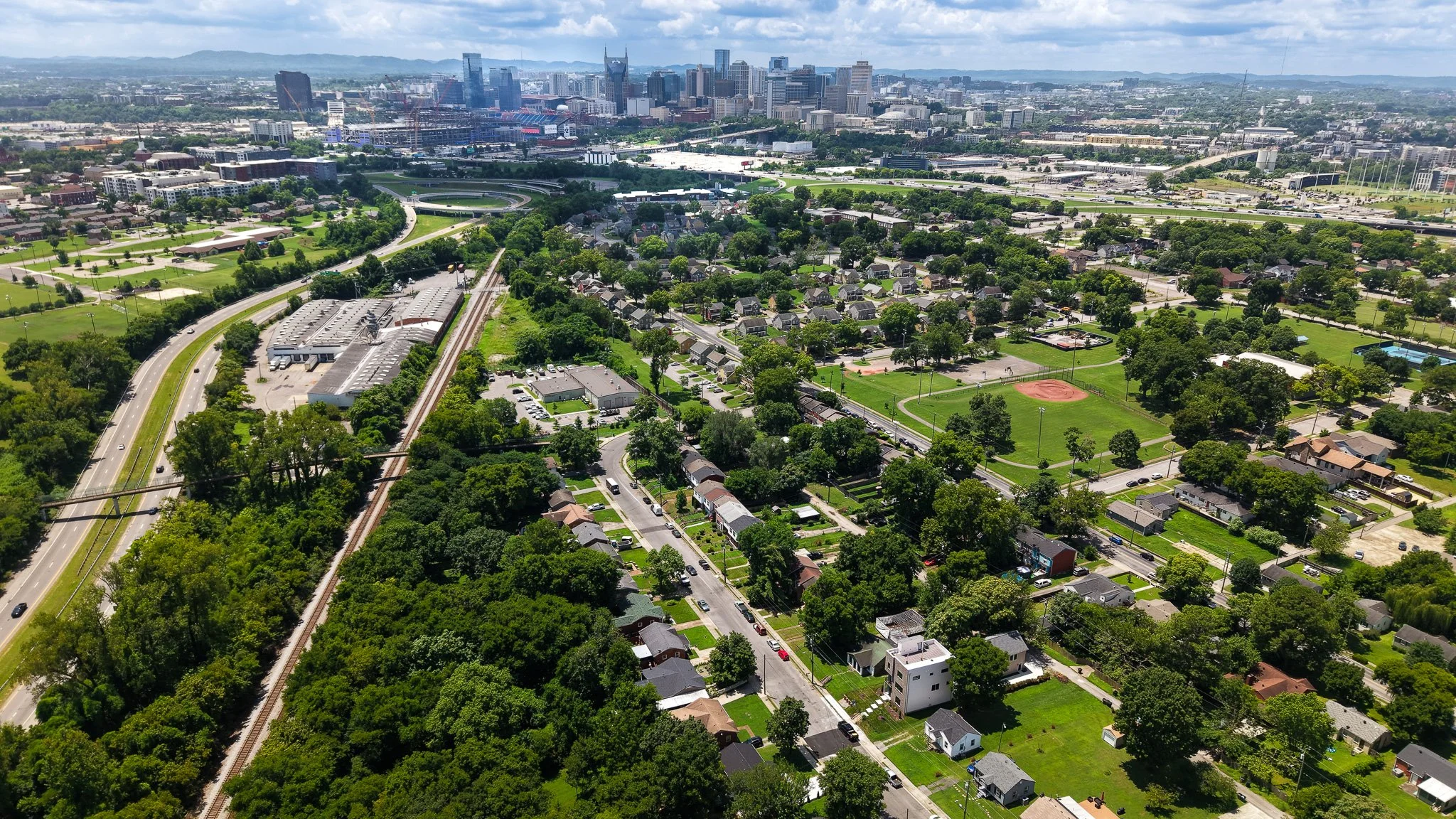Aerial view of a city with a mix of residential neighborhoods, parks, and a skyline of tall Nashville, TN.