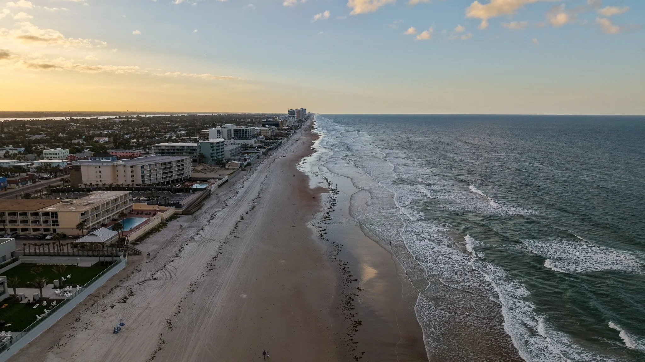 Aerial view of a beachside city at sunset, showing the shoreline, buildings, and ocean waves.