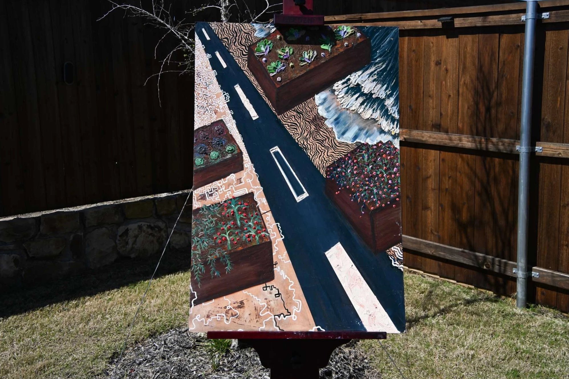 A colorful outdoor display with painted wooden blocks depicting various garden scenes like vegetables, plants, and landscapes, arranged on a board against a wooden fence.