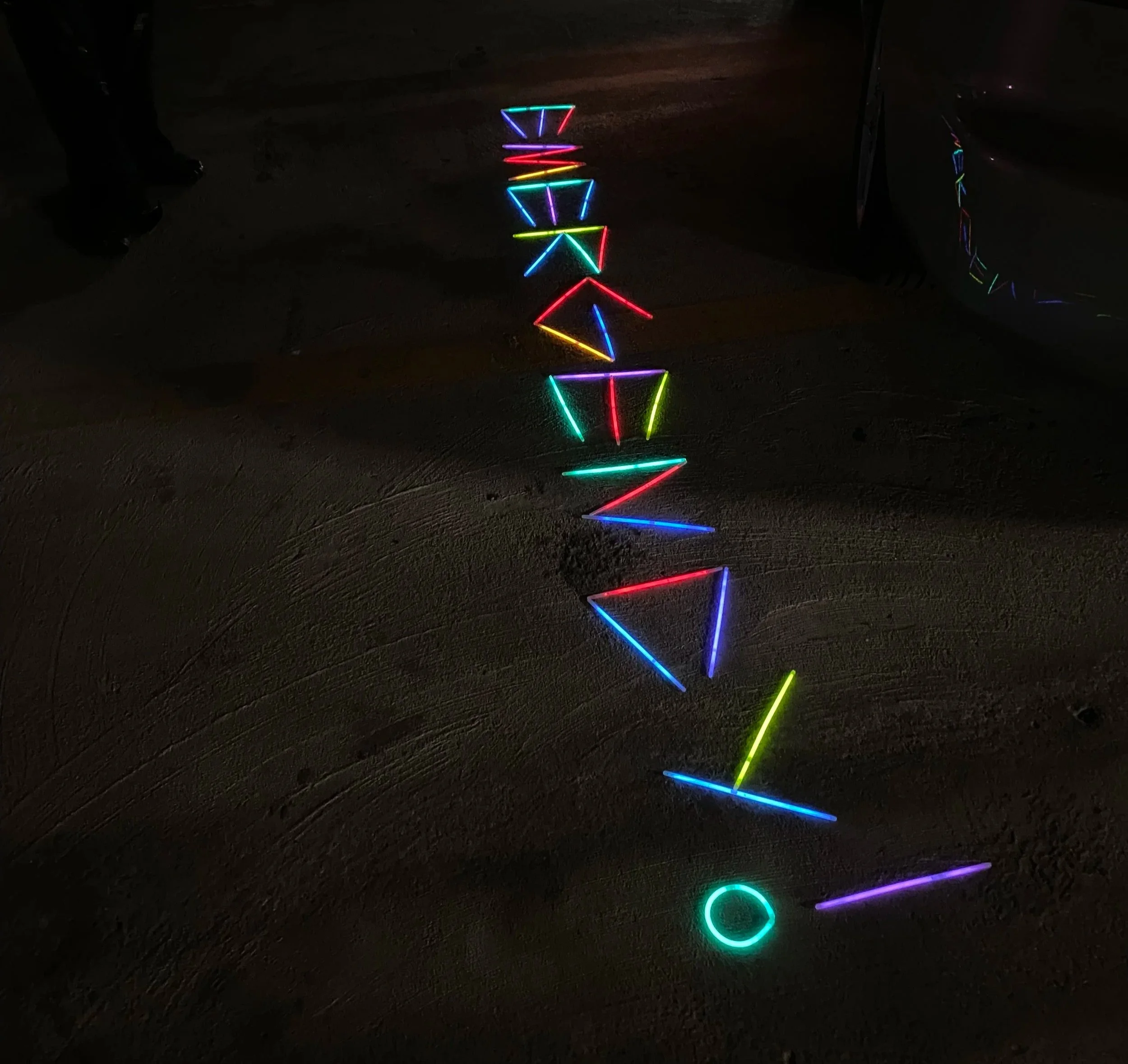 Neon lights arranged in a pattern on the ground, emitting colorful hues of red, green, blue, yellow, and purple in a dark environment.