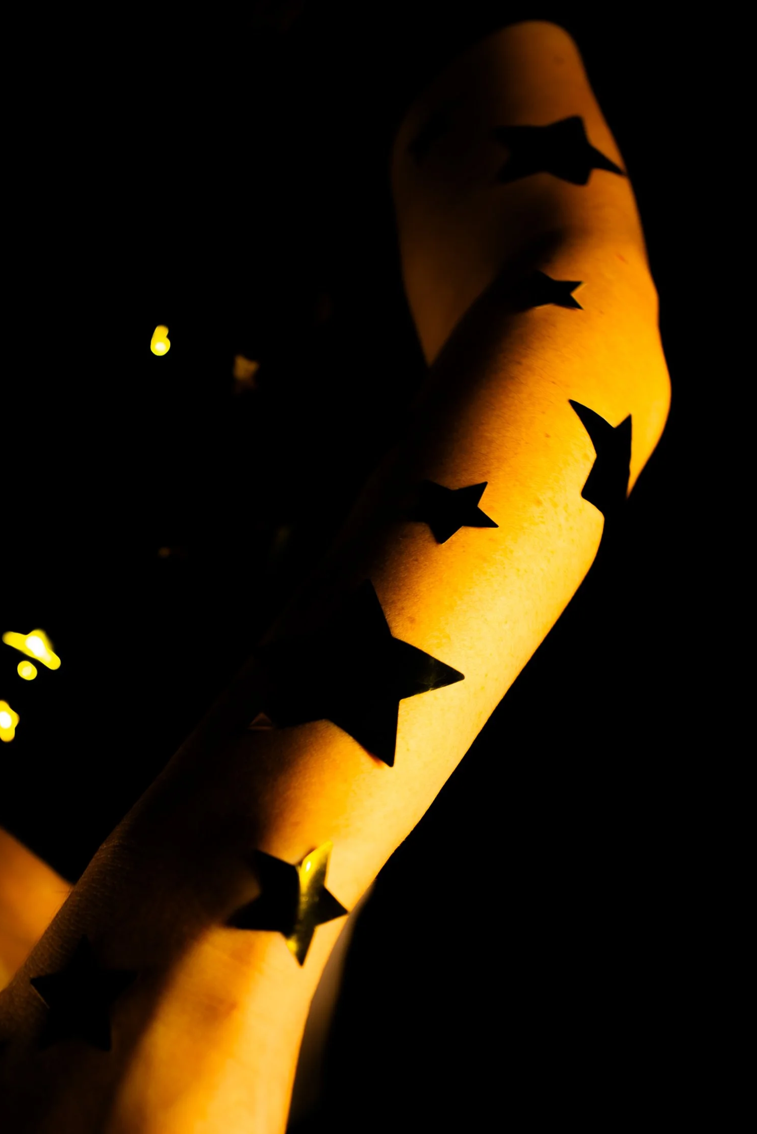 A person's arm illuminated by warm yellow lighting, decorated with star-shaped cutouts.