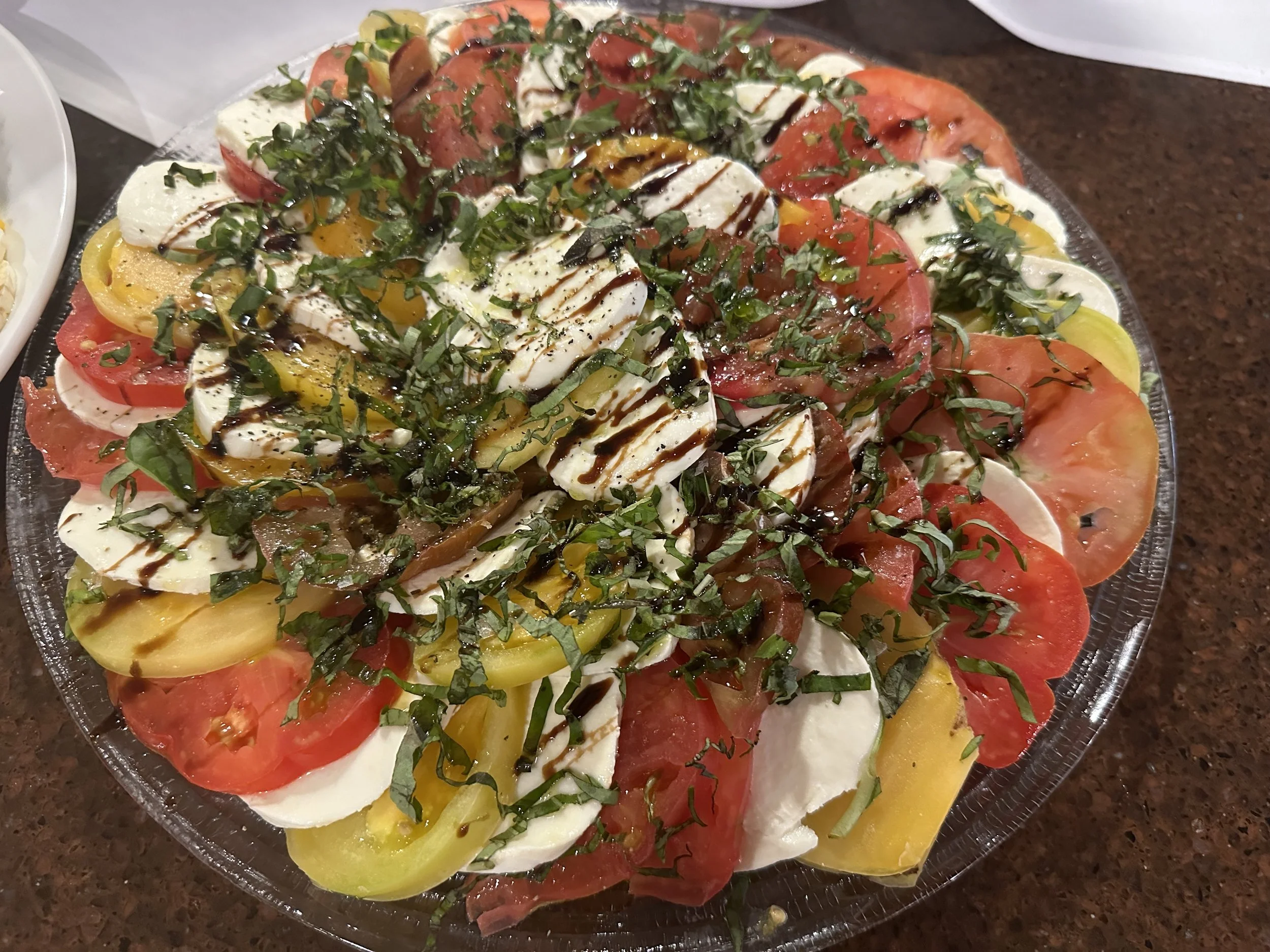 A platter of Caprese salad with sliced tomatoes, mozzarella, basil, balsamic glaze, and olive oil.