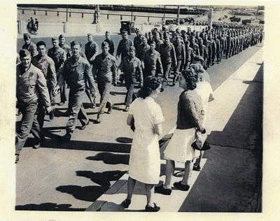 Soldiers march past Australian woman as they disembark off of a ship.
