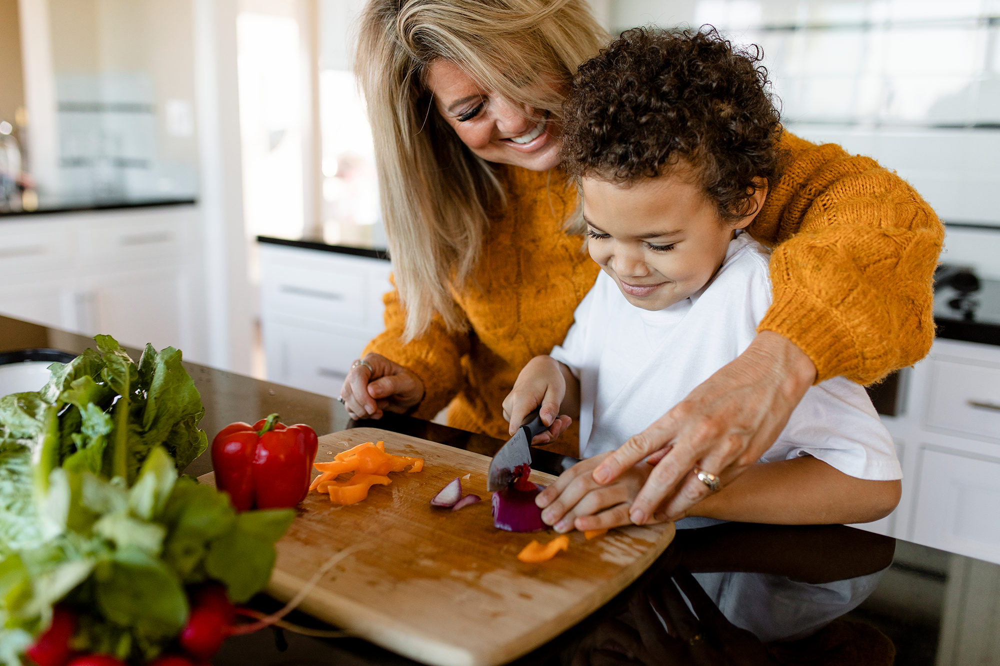 Woman and young boy chopping vegetables together in a bright kitchen.