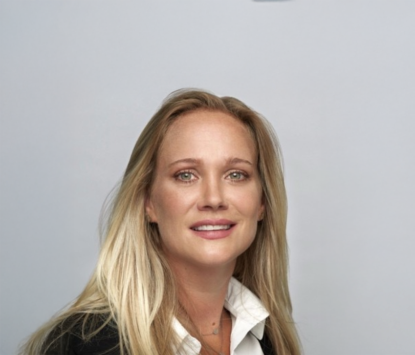 Portrait of a blonde woman with blue eyes smiling against a plain background
