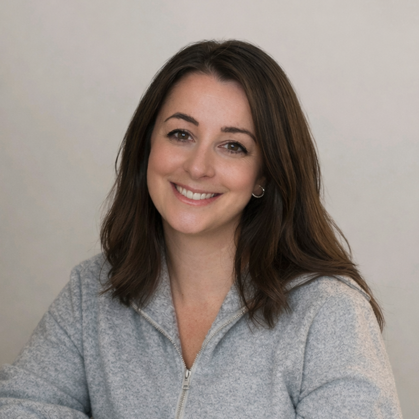 A woman with shoulder-length brown hair smiling, wearing a light gray zip-up sweater, against a plain light-colored background.