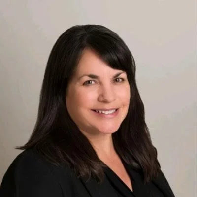 A woman with dark hair smiling at the camera against a plain neutral background.