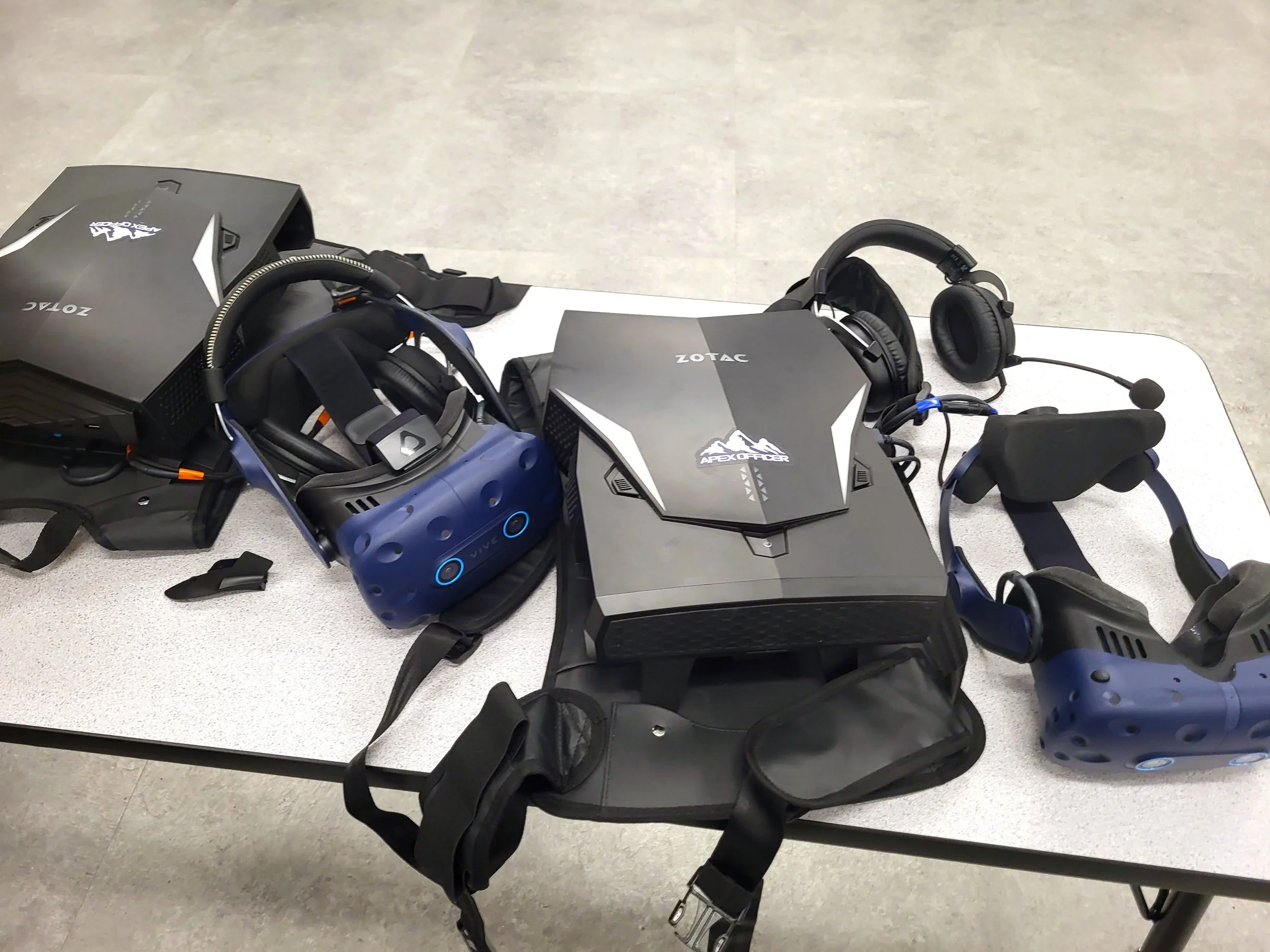 Table with two virtual reality headsets and a gaming controller on a flat surface.