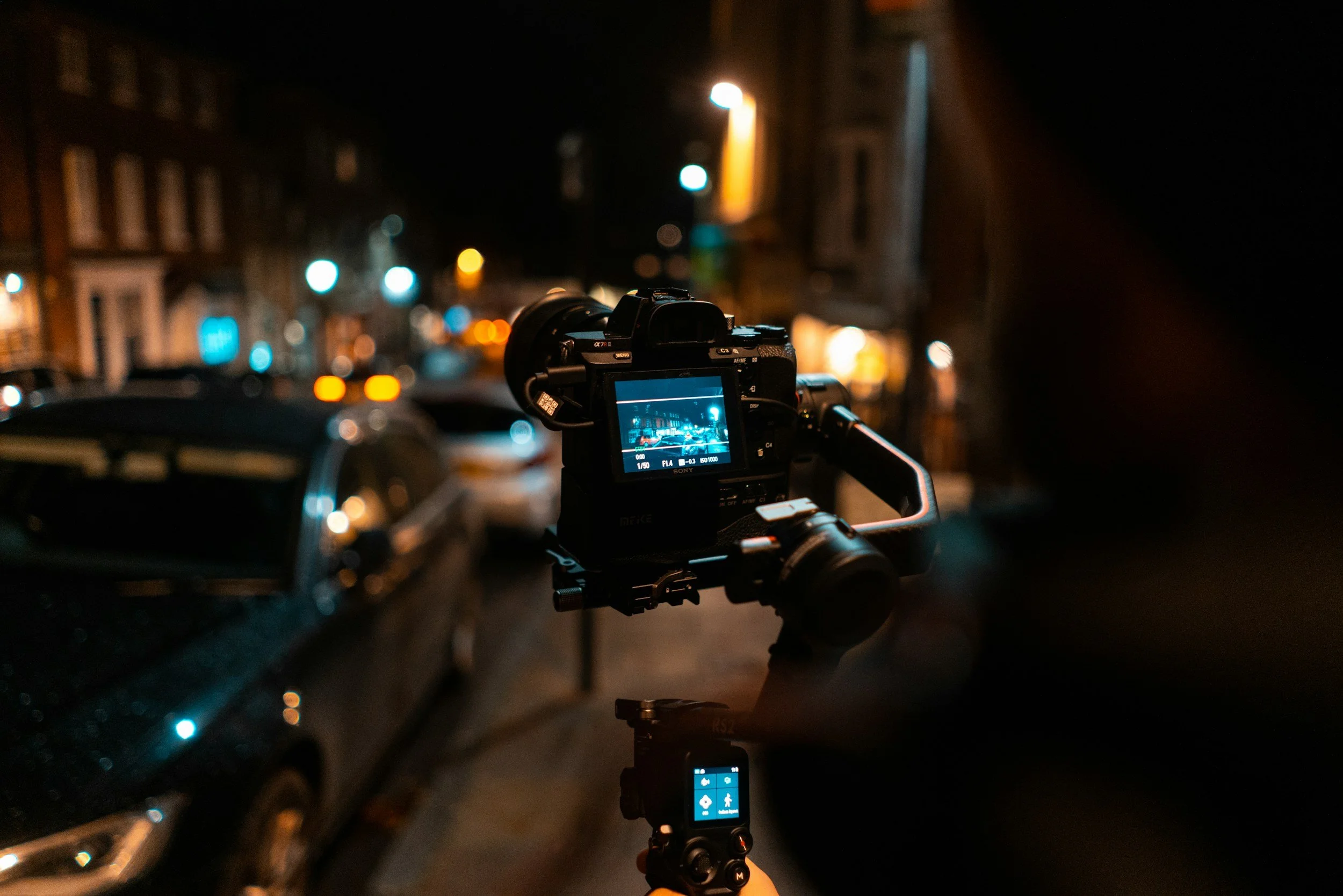 A digital camera on a tripod capturing a shot of a city street at night, with blurry cars and streetlights in the background.