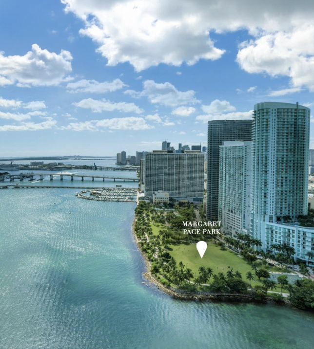 Aerial view of Margaret Pace Park with high-rise buildings and water in Miami, Florida, under a partly cloudy sky.