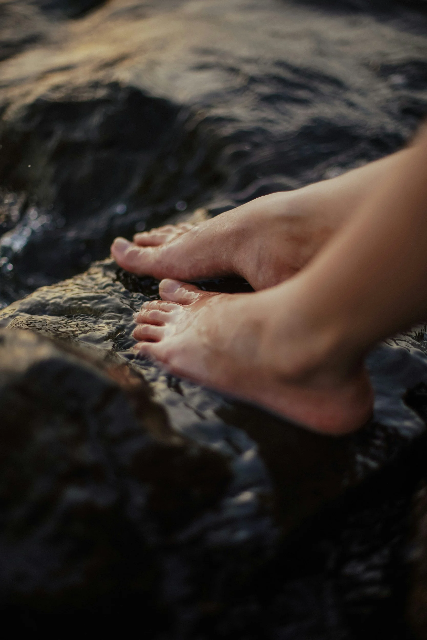 Close-up of two bare feet touching wet rocks in a river or stream with flowing water.
