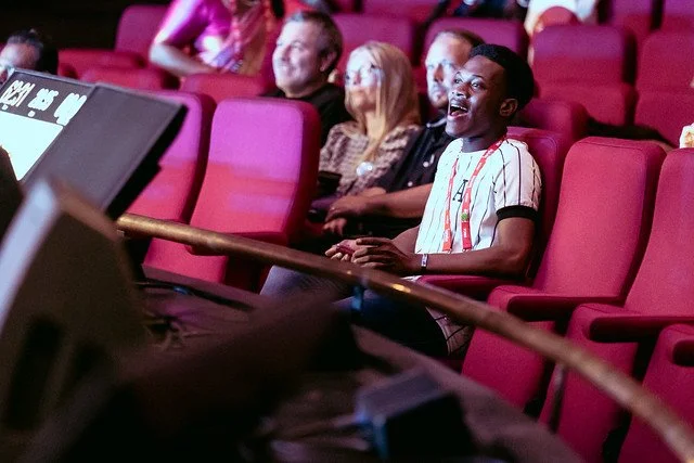 A group of people sitting in red theater seats, laughing and enjoying a performance.