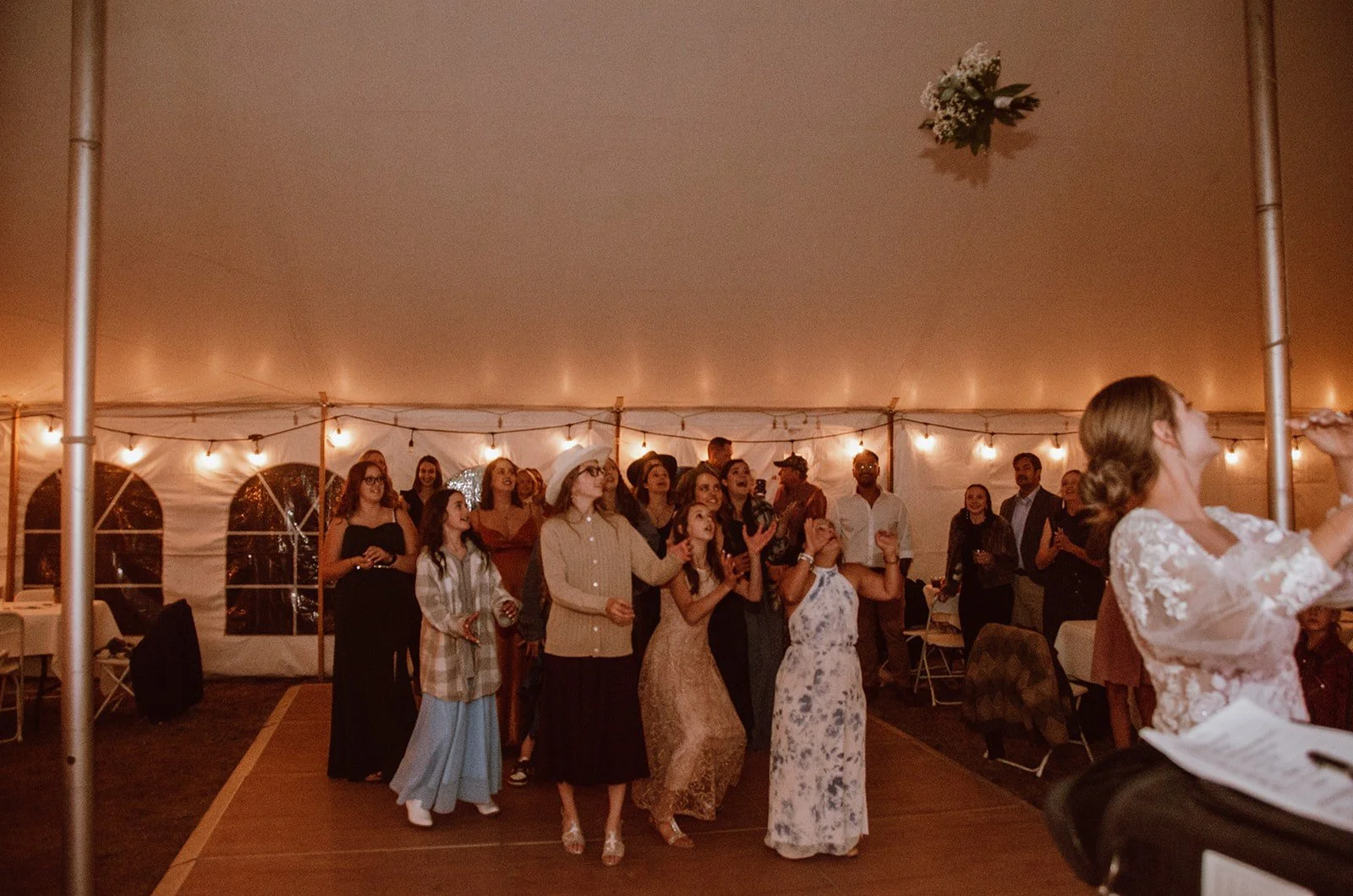 Two massage therapists prepare a tranquil retreat space in a geodome with lush greenery visible through large, geometric windows. The setup includes cozy massage tables and soft, ambient lighting.