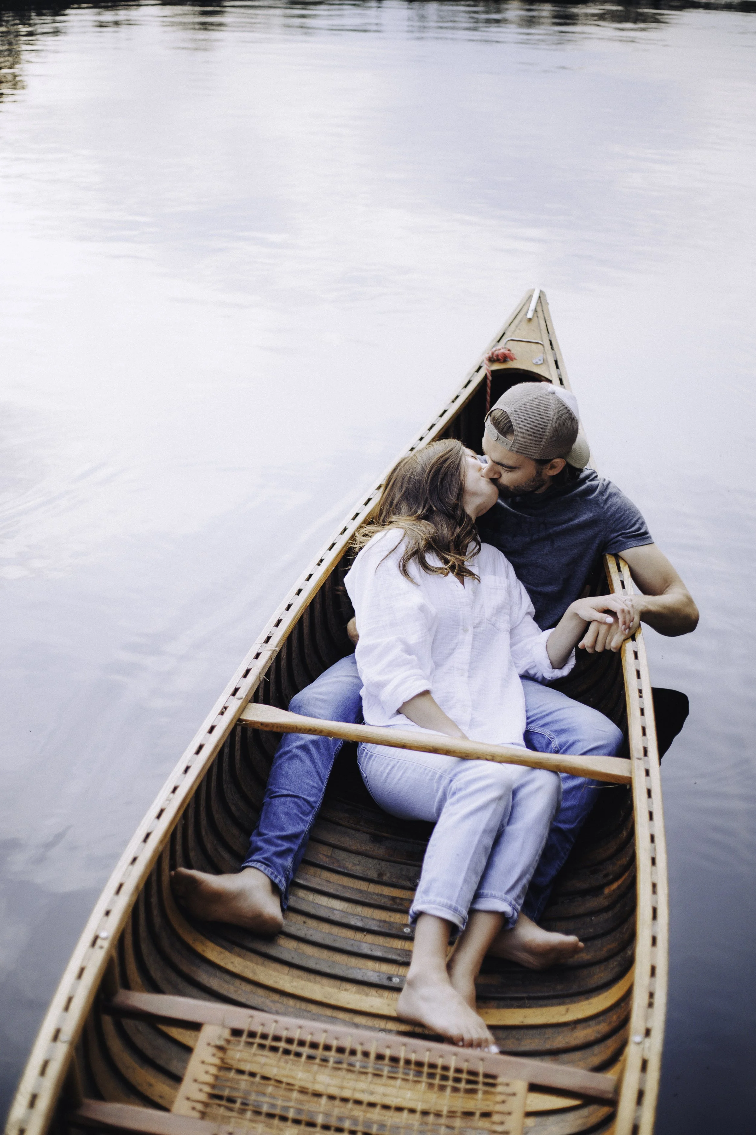 A couple sharing a kiss while sitting in a canoe on a calm lake.