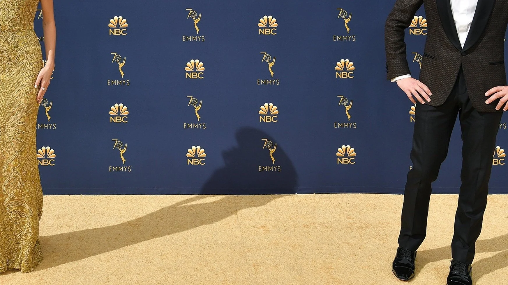 Part of a red carpet event with two people in formal attire and a blue backdrop with Emmy and NBC logos