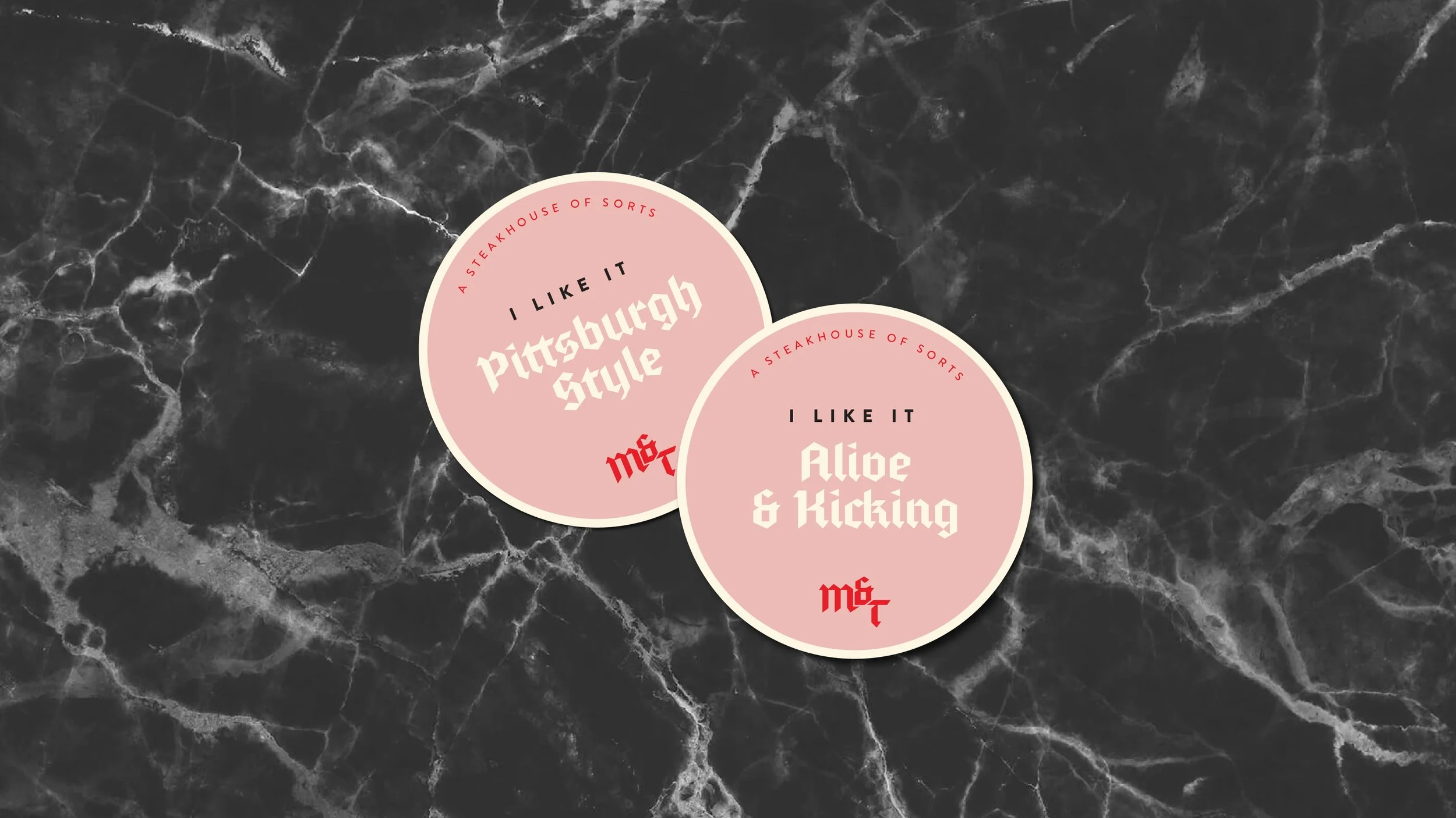 Two pink circular stickers on a black marble surface. The left sticker says 'I LIKE IT Pittsburgh Style' and the right sticker says 'I LIKE IT Alice & Kicking.' Both have 'A STEAKHOUSE OF SORTS' written around the top edge.