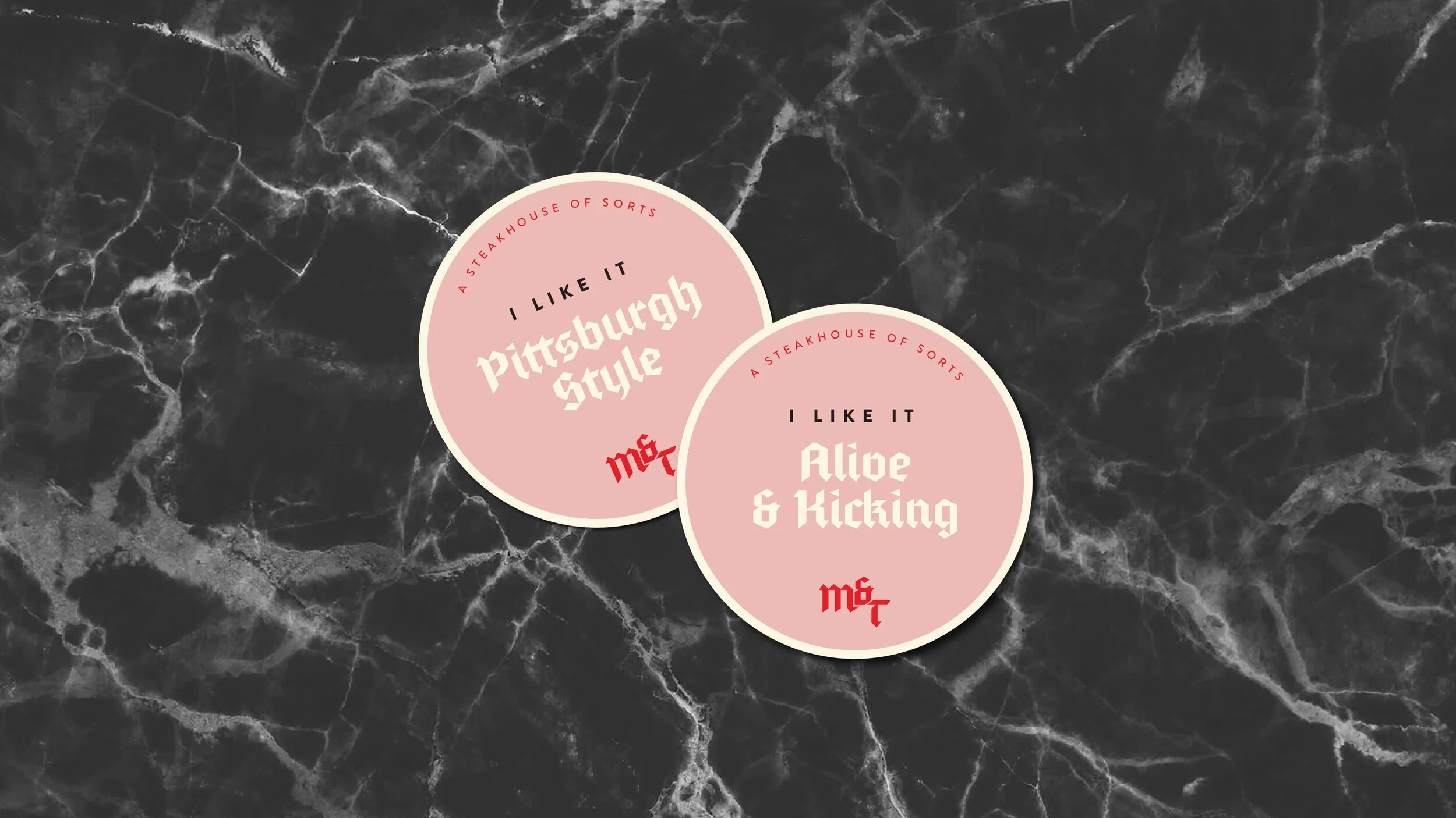 Two pink circles with white borders on a black marble background. The left circle says "I LIKE IT Pittsburgh Style" and the right circle says "I LIKE IT Alice & Kicking." Both circles have the phrase "A STEAKHOUSE OF SORTS" written in small red text around the top edge. There is a red logo "MF" at the bottom of each circle.