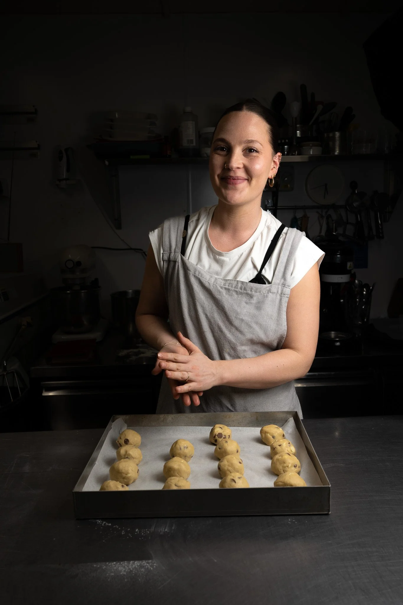 A woman standing behind a baking tray with cookie dough balls, in a kitchen setting.
