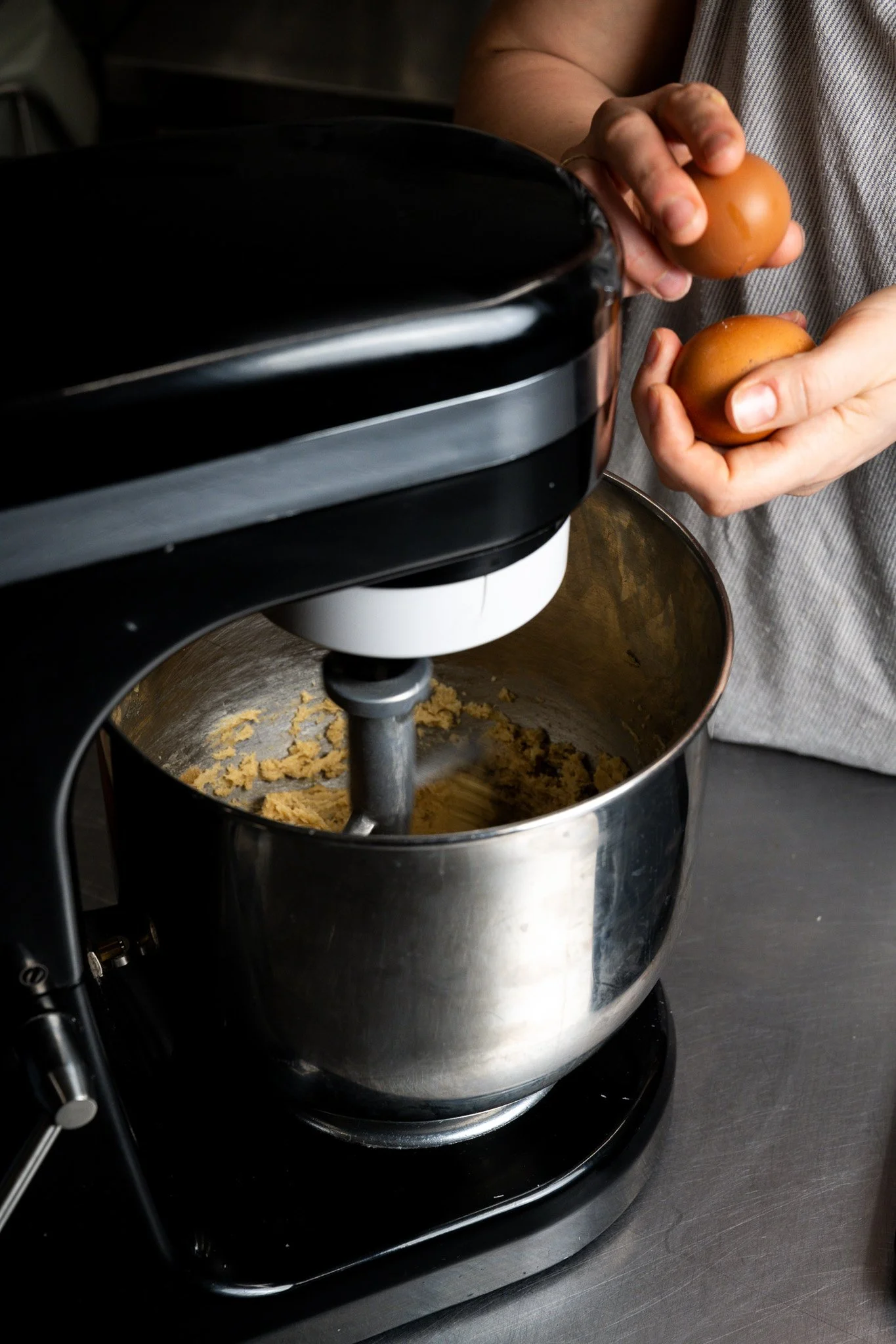 Person adding eggs to a stand mixer with cookie dough inside.