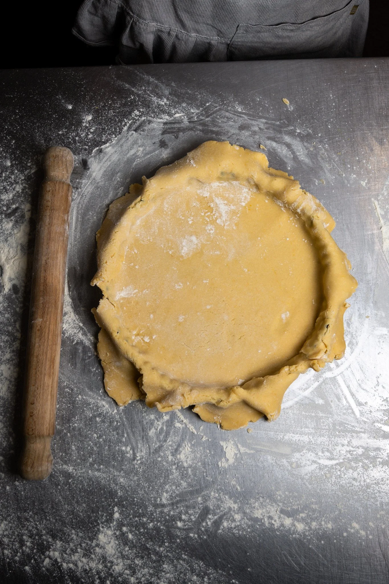 Unrolled pie crust on a floured metal surface with a rolling pin nearby.