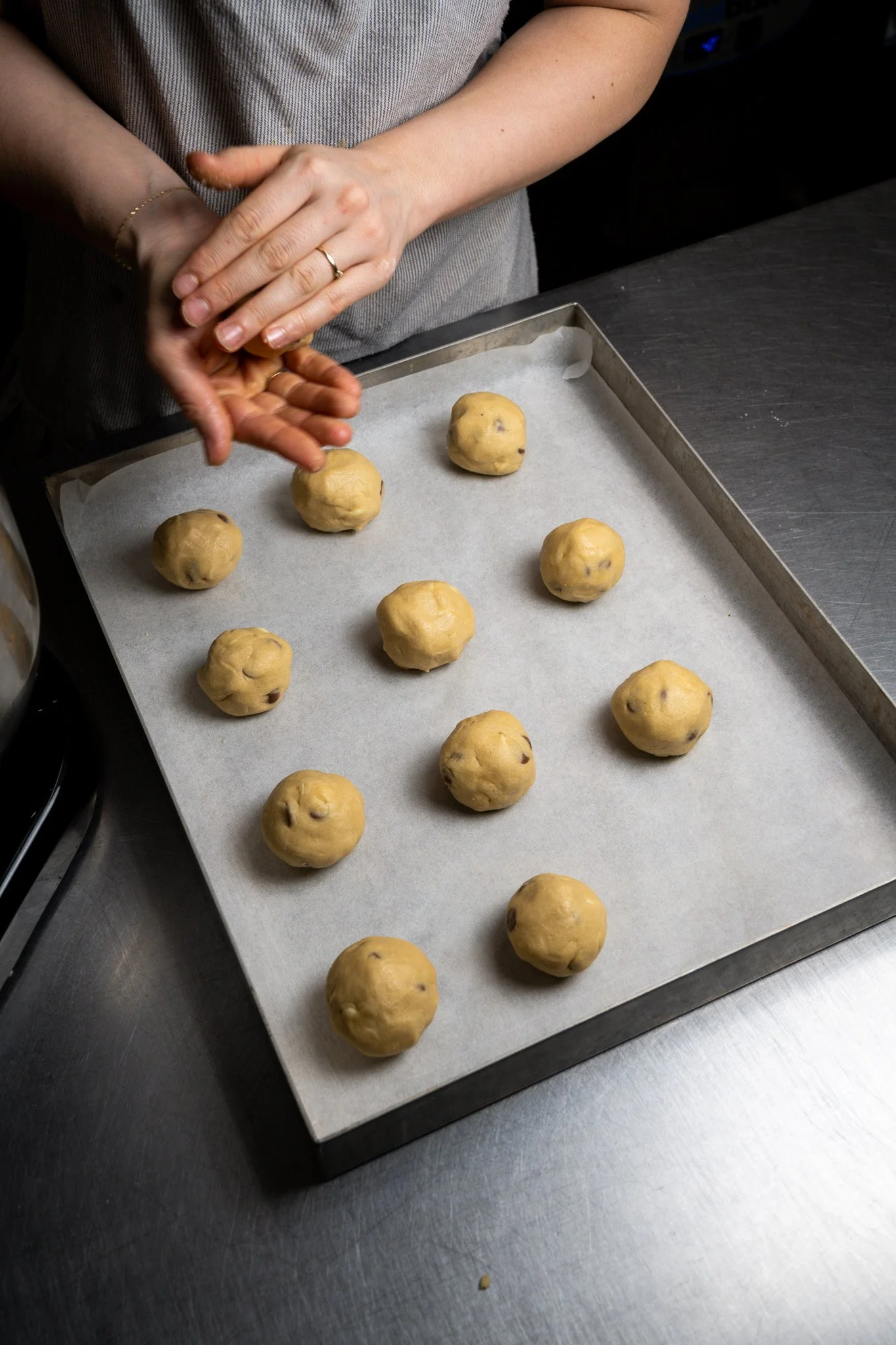 Person preparing cookie dough balls on a baking sheet lined with parchment paper.