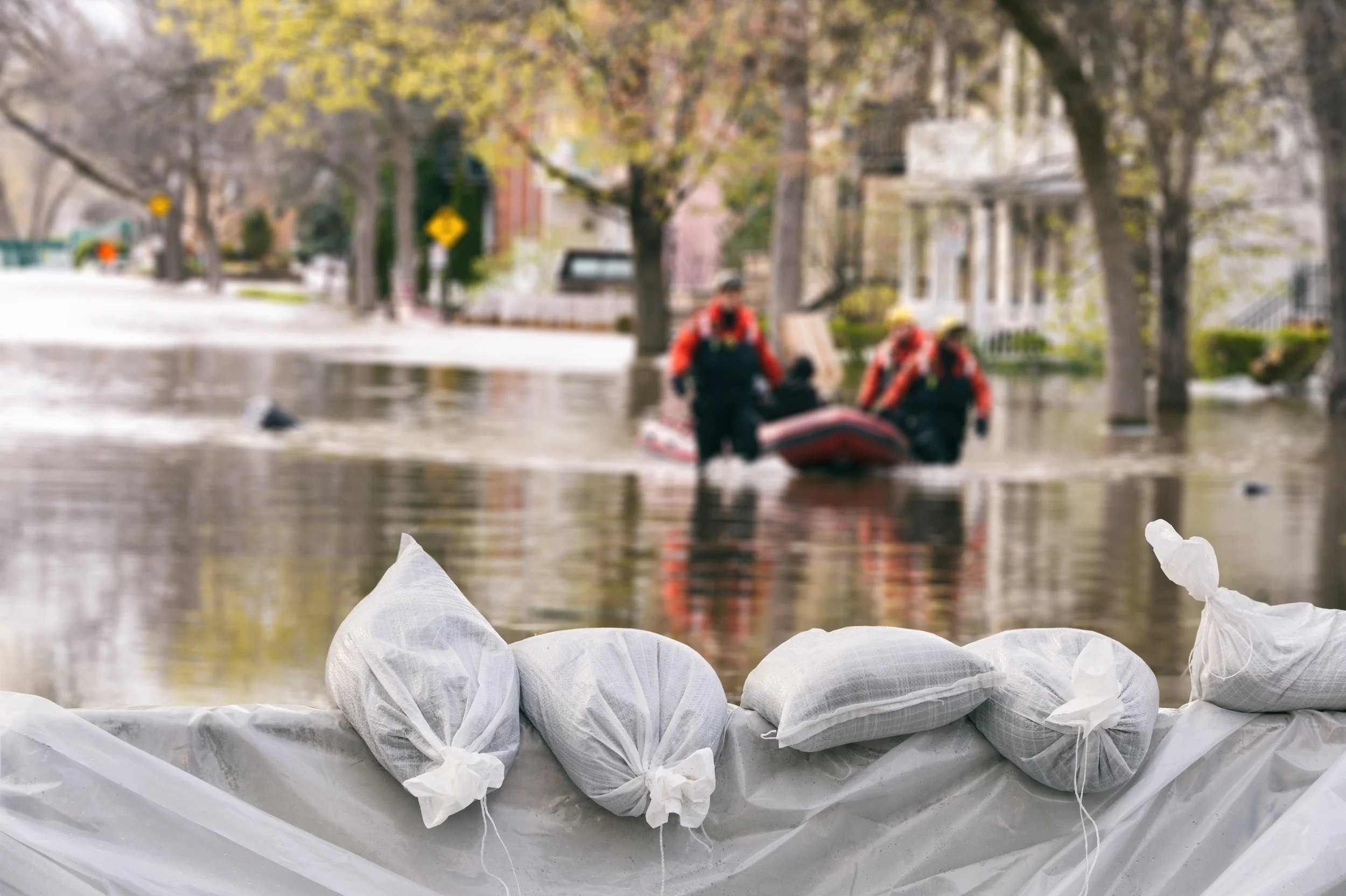 Sandbags lined up in front of a flooded street with rescue workers in a boat in the background