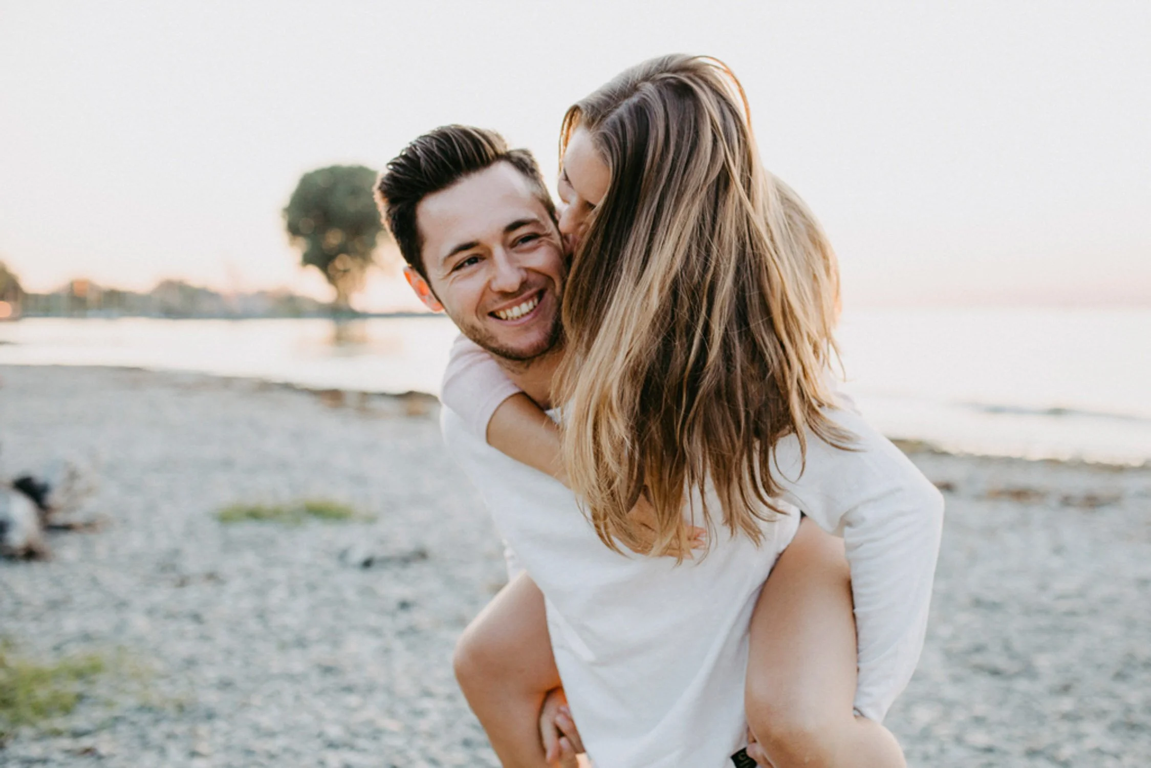 Ein lachendes Paar am Strand, der Mann trägt das Mädchen auf dem Rücken.
