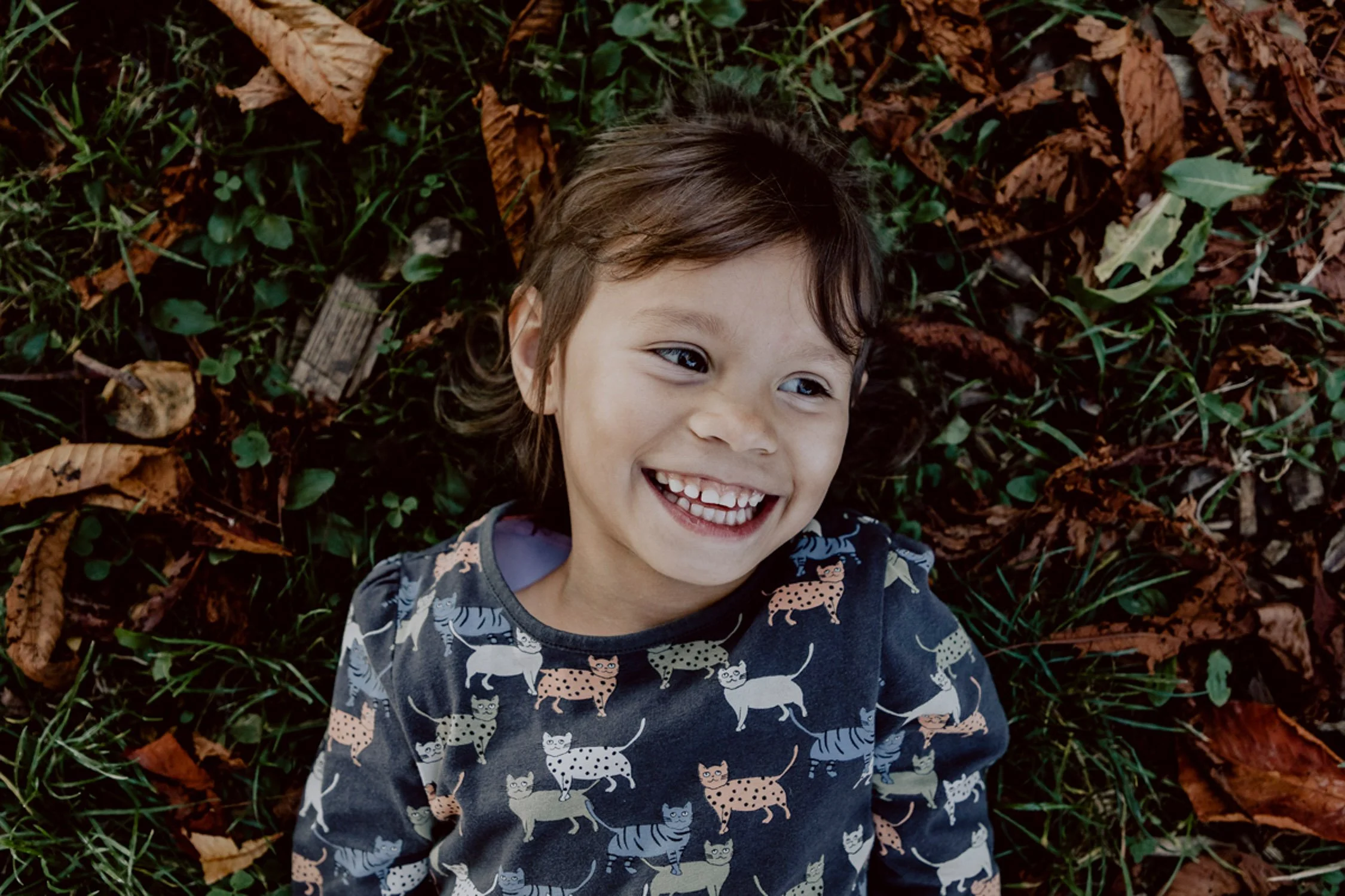 Ein lachendes Mädchen liegt auf einem Laubhaufen im Freien.