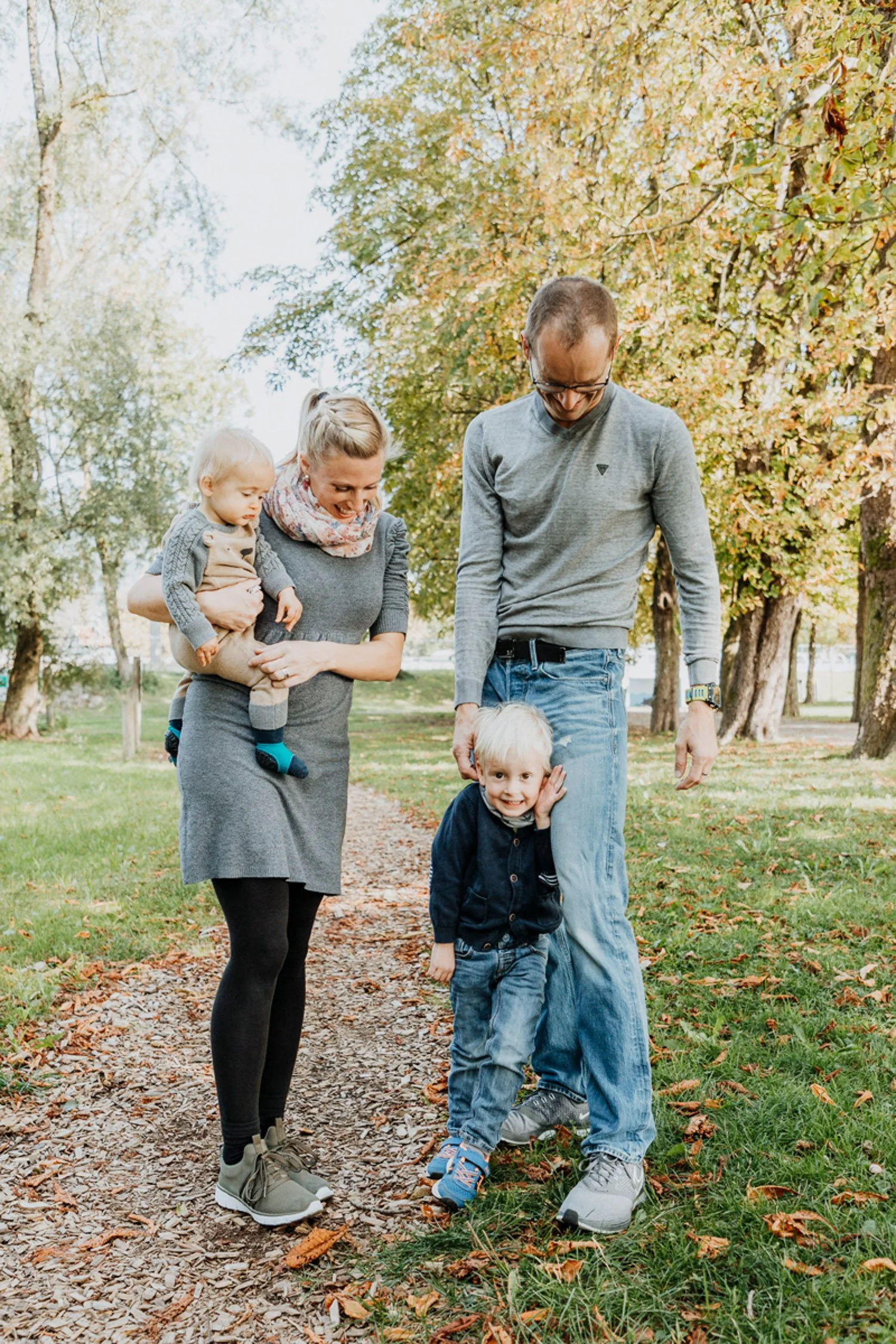 Familie mit zwei Kindern beim Spaziergang im Park im Herbst, bunte Blätter auf dem Boden und Bäume mit Herbstlaub.