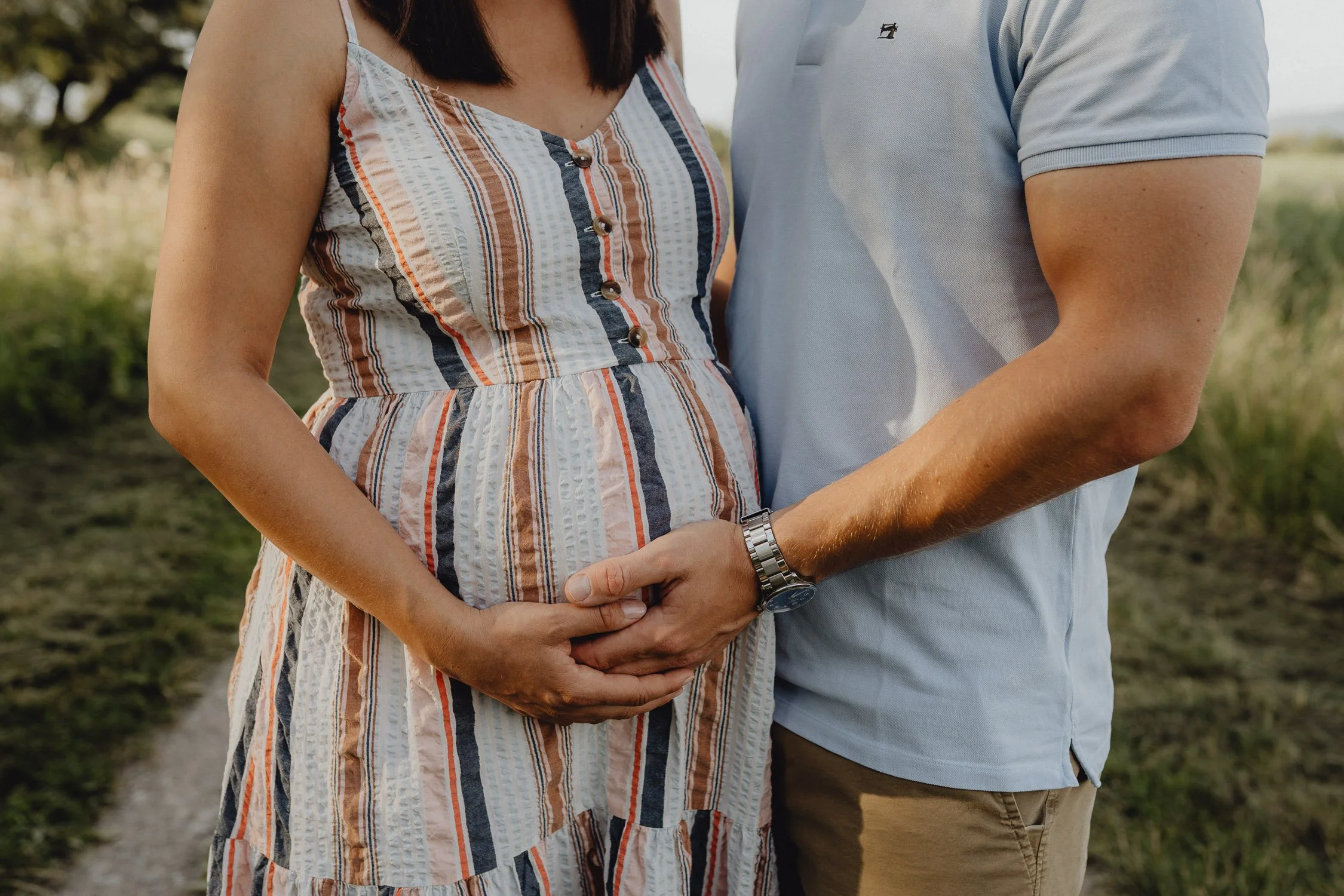 Ein Paar hält liebevoll die Hände auf den Babybauch während eines Spaziergangs im Freien.