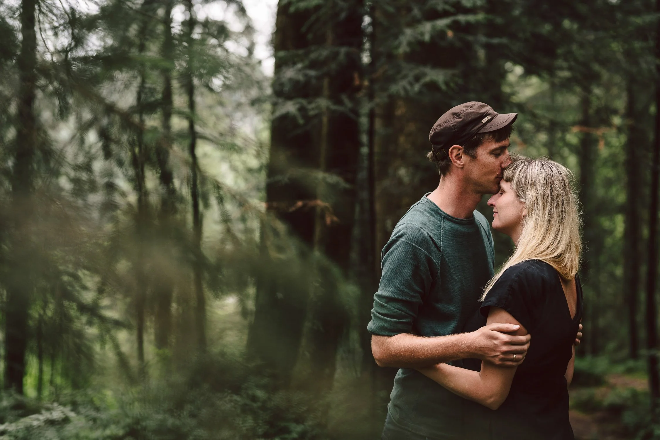 Ein Paar umarmt sich in einemwald, der Mann küsst die Frau auf die Stirn.