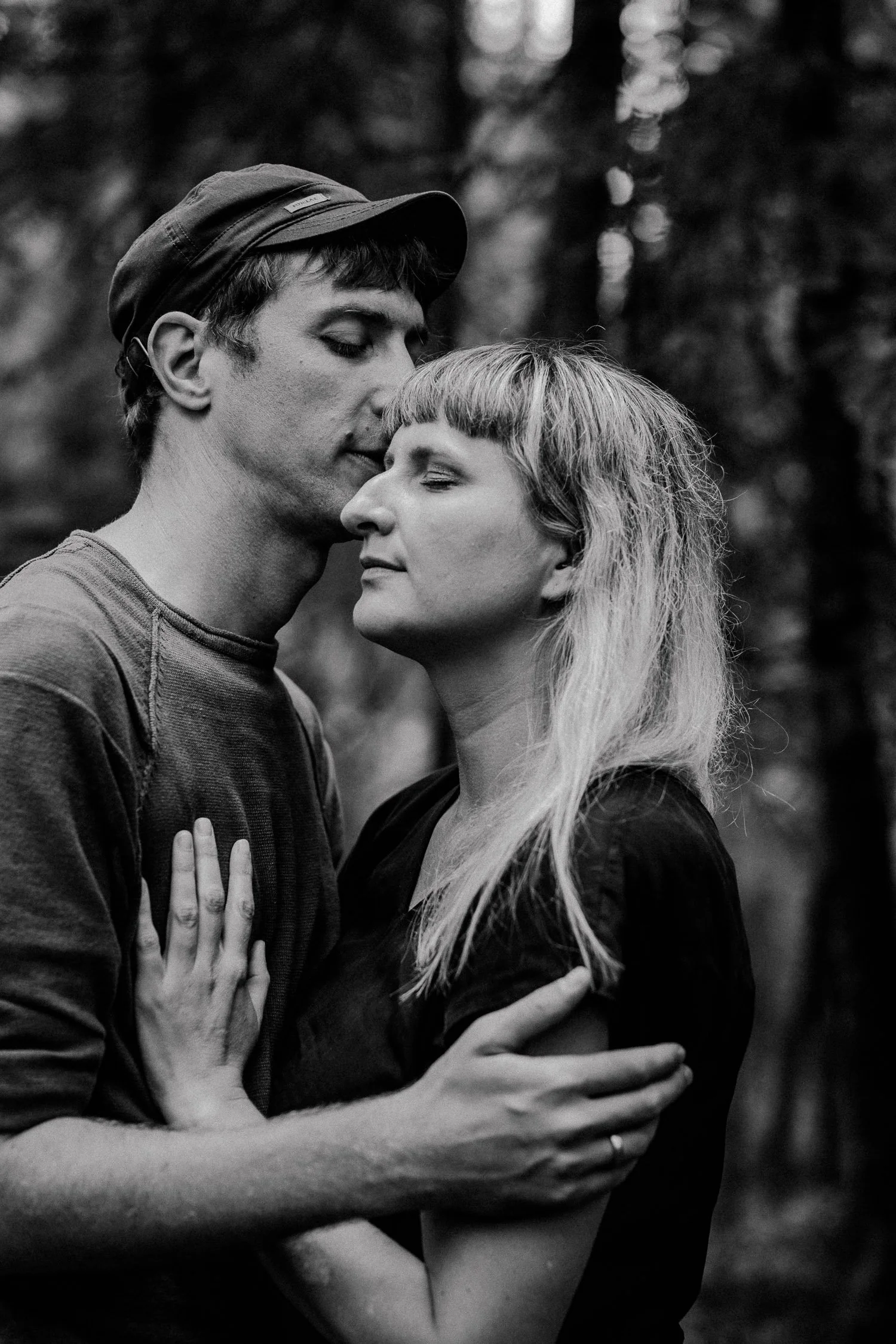 Schwarz-Weiß-Foto eines Paares, das sich liebevoll umarmt, mit den Augen geschlossen, in einem Wald.