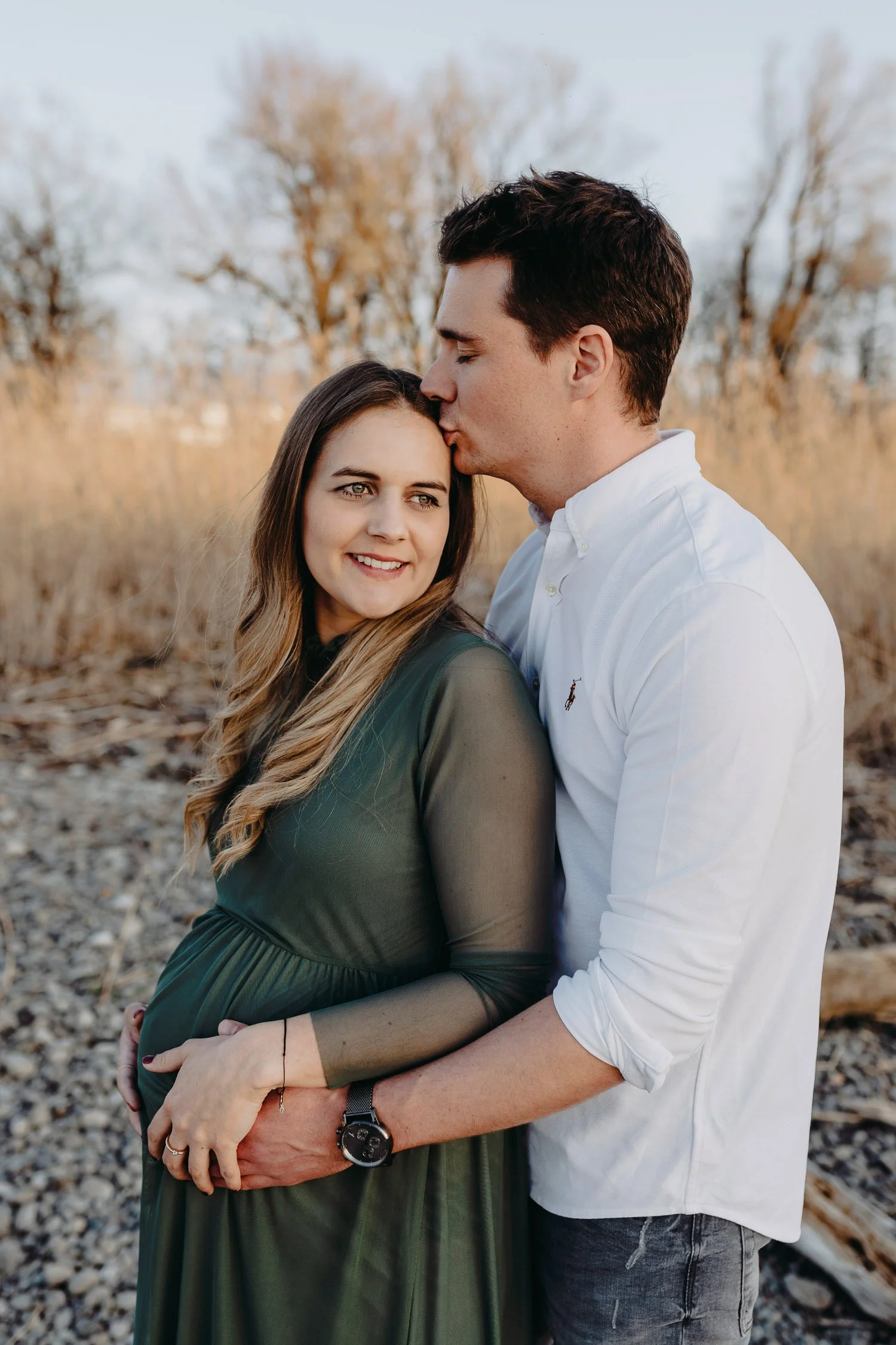 Ein Paar, das sich liebevoll in einer Naturumgebung umarmt, der Mann küsst die Frau auf die Stirn.