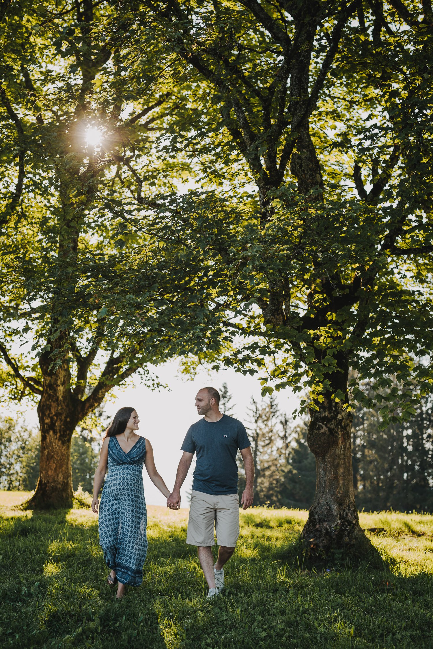 Ein Paar geht Hand in Hand auf einer Wiese unter Bäumen an einem sonnigen Tag.