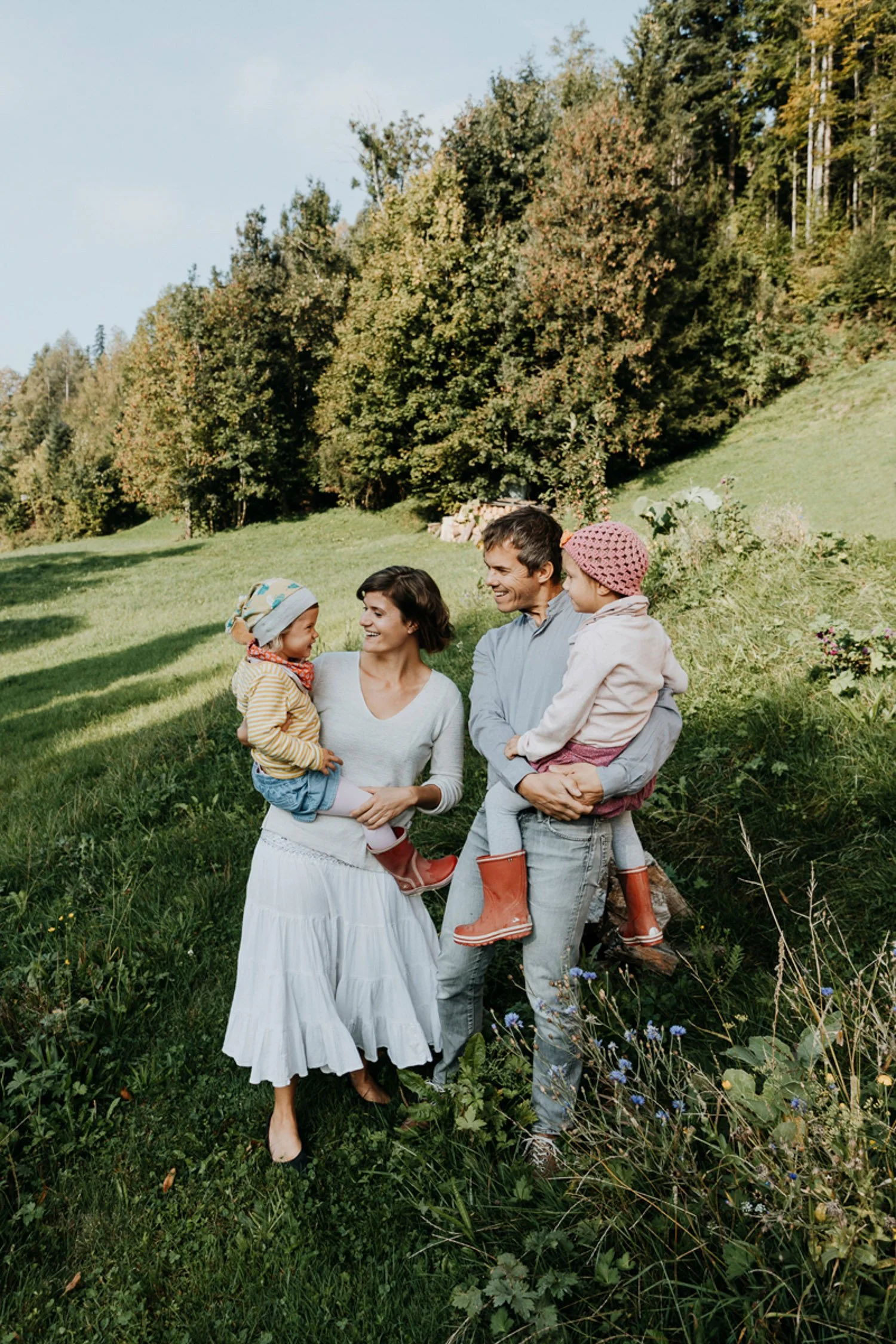 Familie mit zwei Kindern im Grünen, lachend und spielend in einer Naturumgebung mit Bäumen und Wiese.