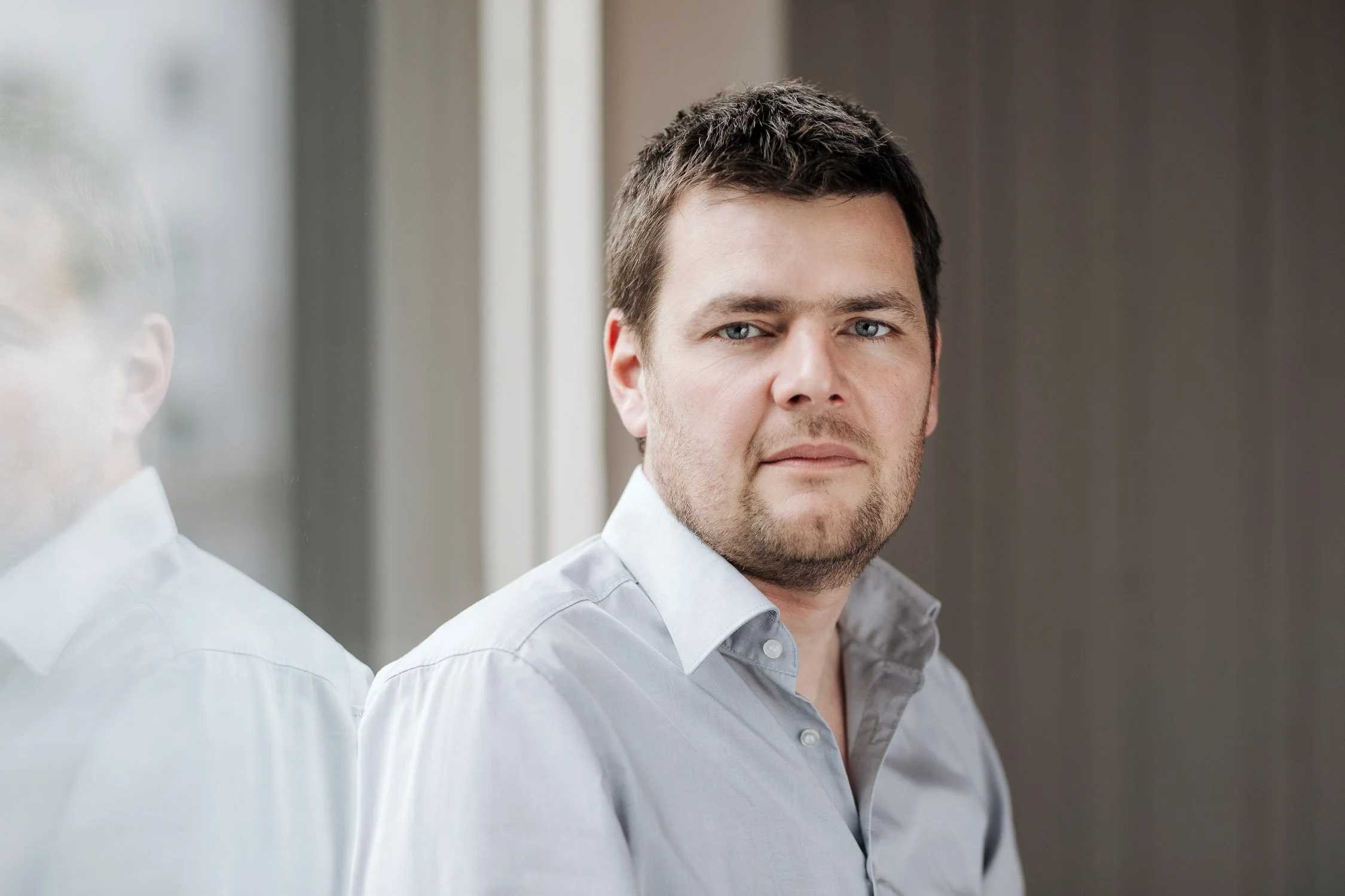 Junger Mann in hellem Hemd schaut nach vorne an einem Fenster.