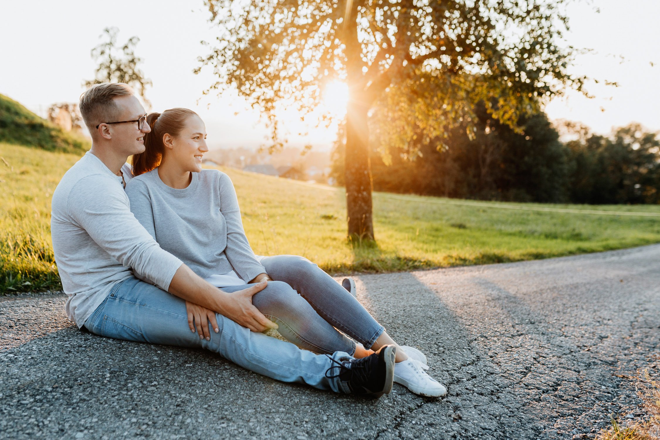 Ein Paar sitzt entspannt auf dem Boden neben einem Baum im Sonnenuntergang in der Natur.