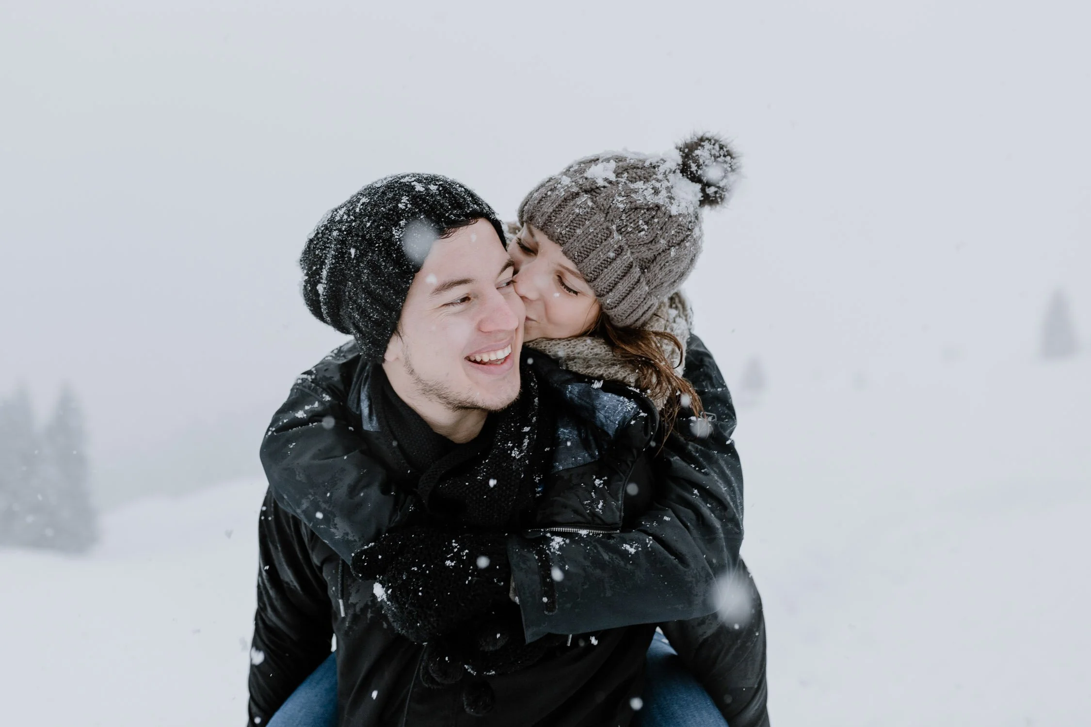 Ein lächelndes Paar in Winterkleidung, umgeben von Schneefall, bei einem Spaziergang im Schnee.