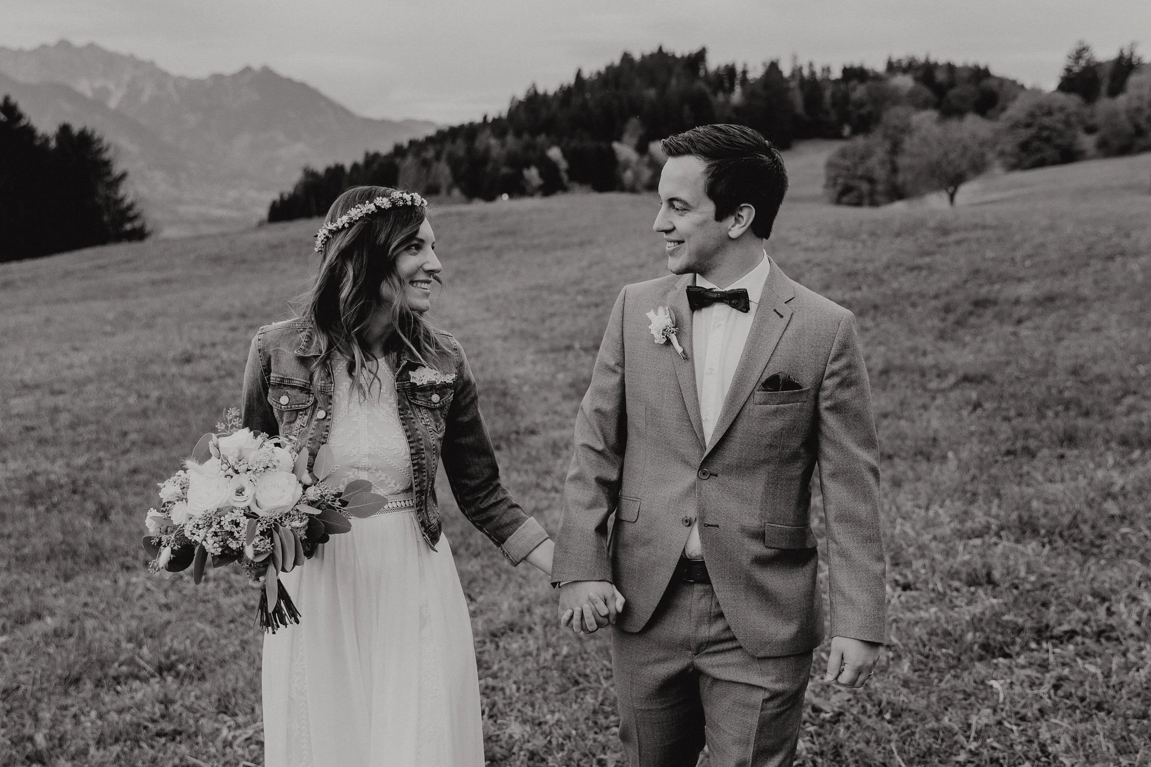 Ein brautpaar hält Händchen im Grünen, beim Spaziergang in den Bergen, im schwarzen-weißen Foto.