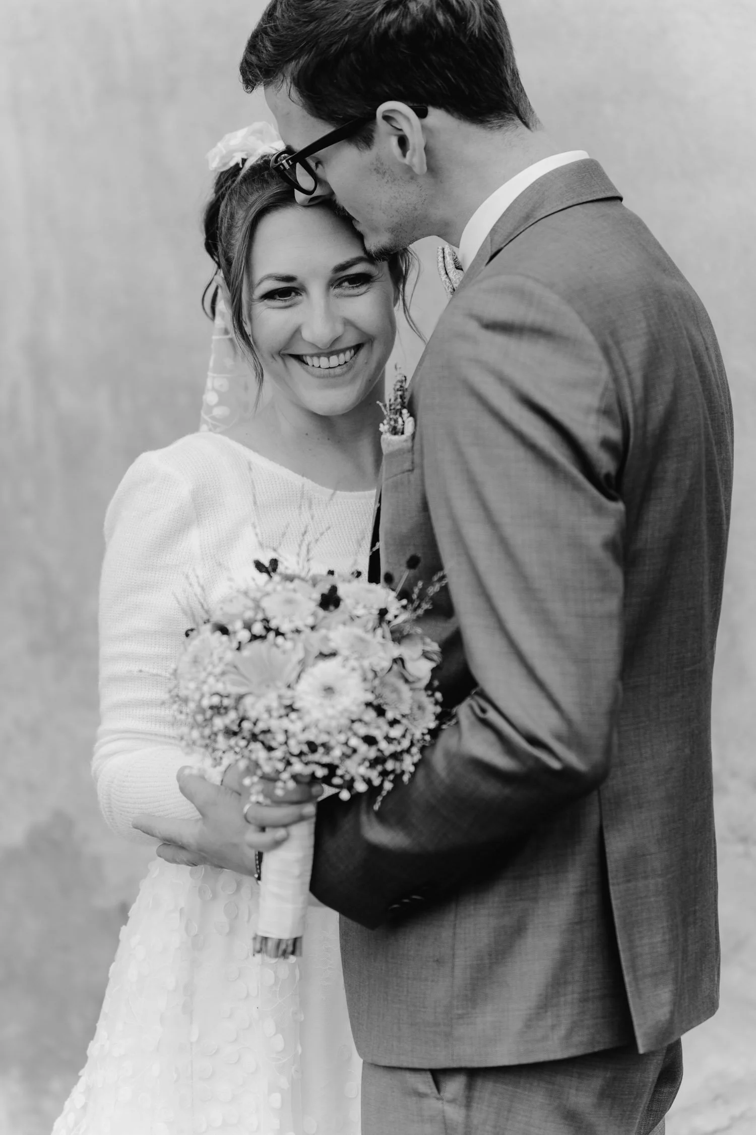 Braut und Bräutigam lächeln sich bei ihrer Hochzeit an, die Braut hält einen Blumenstrauß.