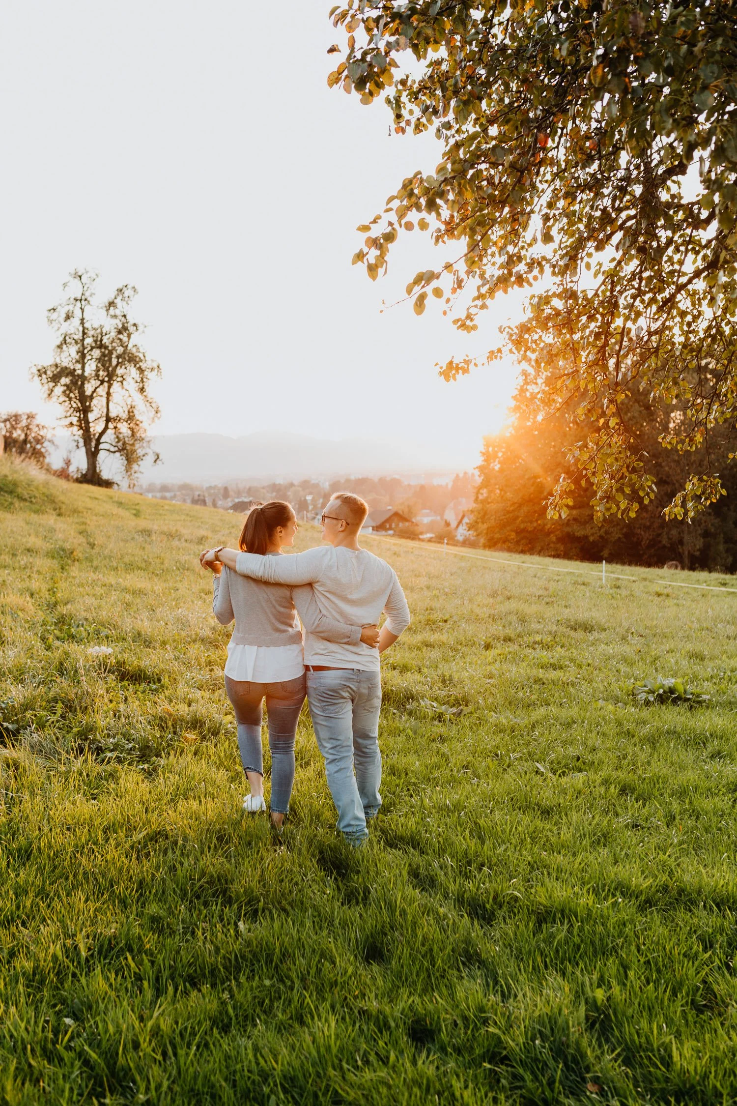 Paar spaziert im Grünen bei Sonnenuntergang, umarmt sich, Natur, Bäume, Wiese, ländliche Gegend, romantische Atmosphäre.