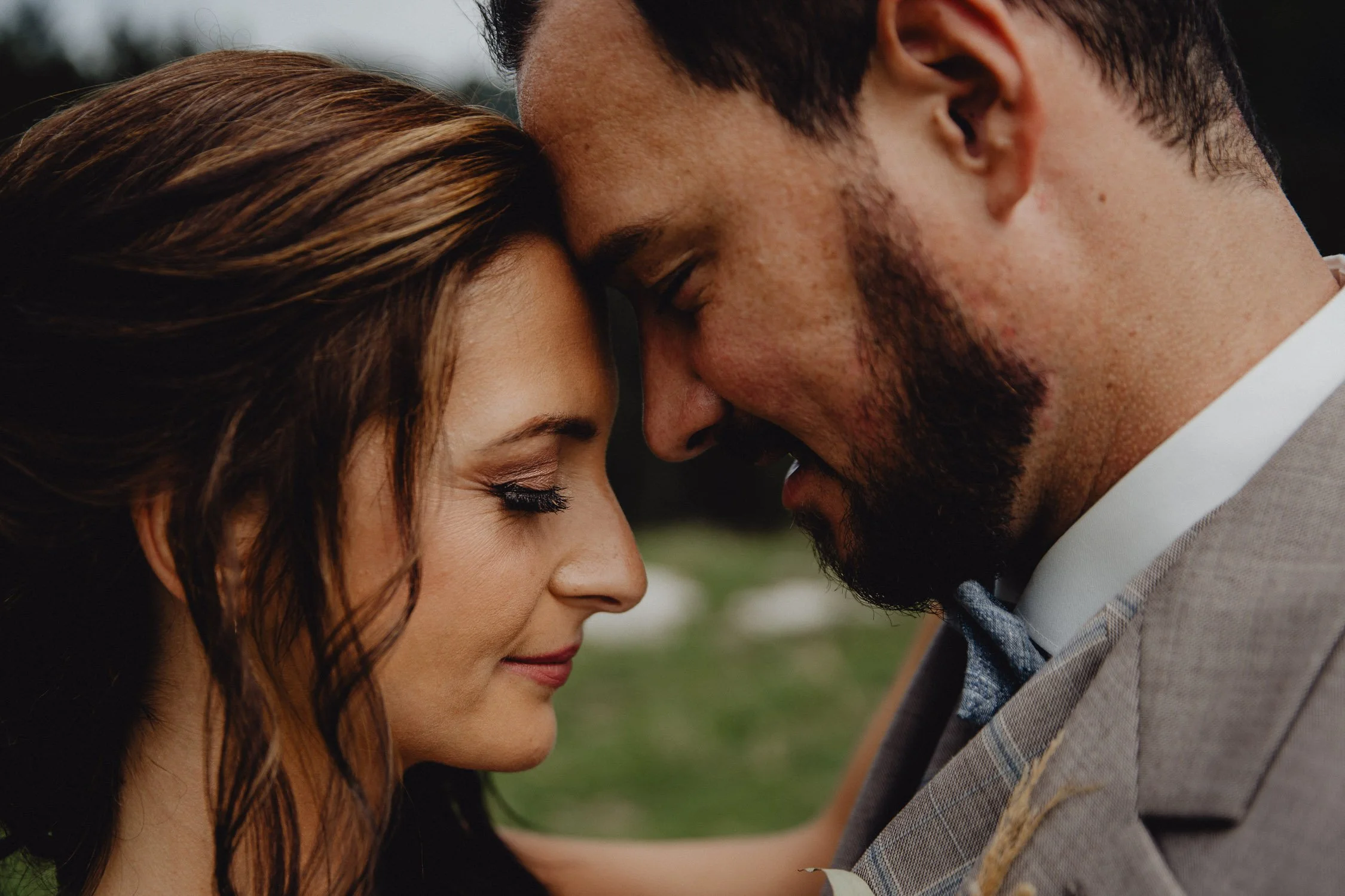 Ein Paar steht mit vorangeschobenen Köpfen, ihre Stirn aneinander, in einer innigen Umarmung im Freien.