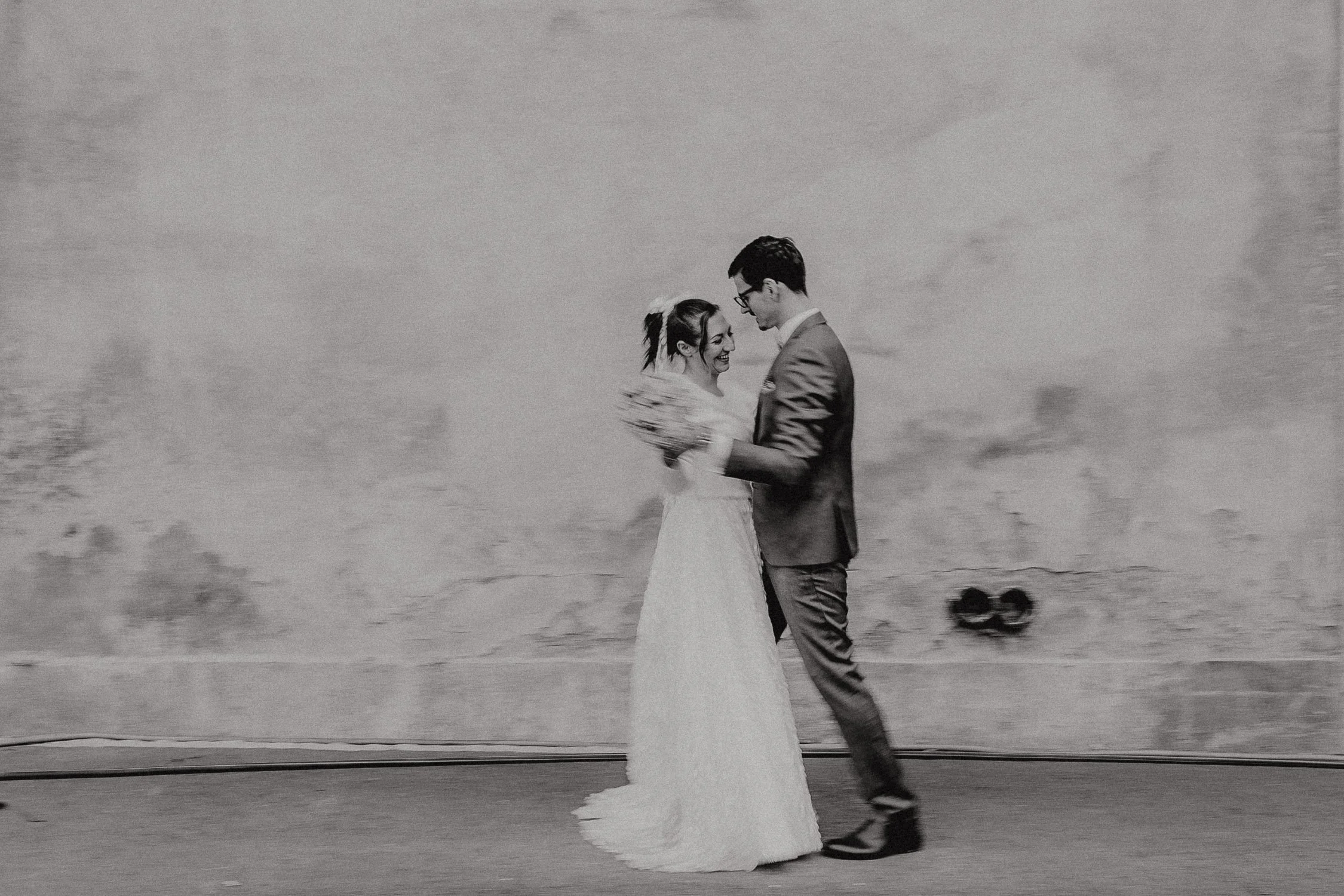 Ein Brautpaar tanzt an der Wand des Hintergrunds, in Schwarz-Weiß. Das Paar lächelt sich an, die Braut trägt ein langes Kleid, der Bräutigam einen Anzug.