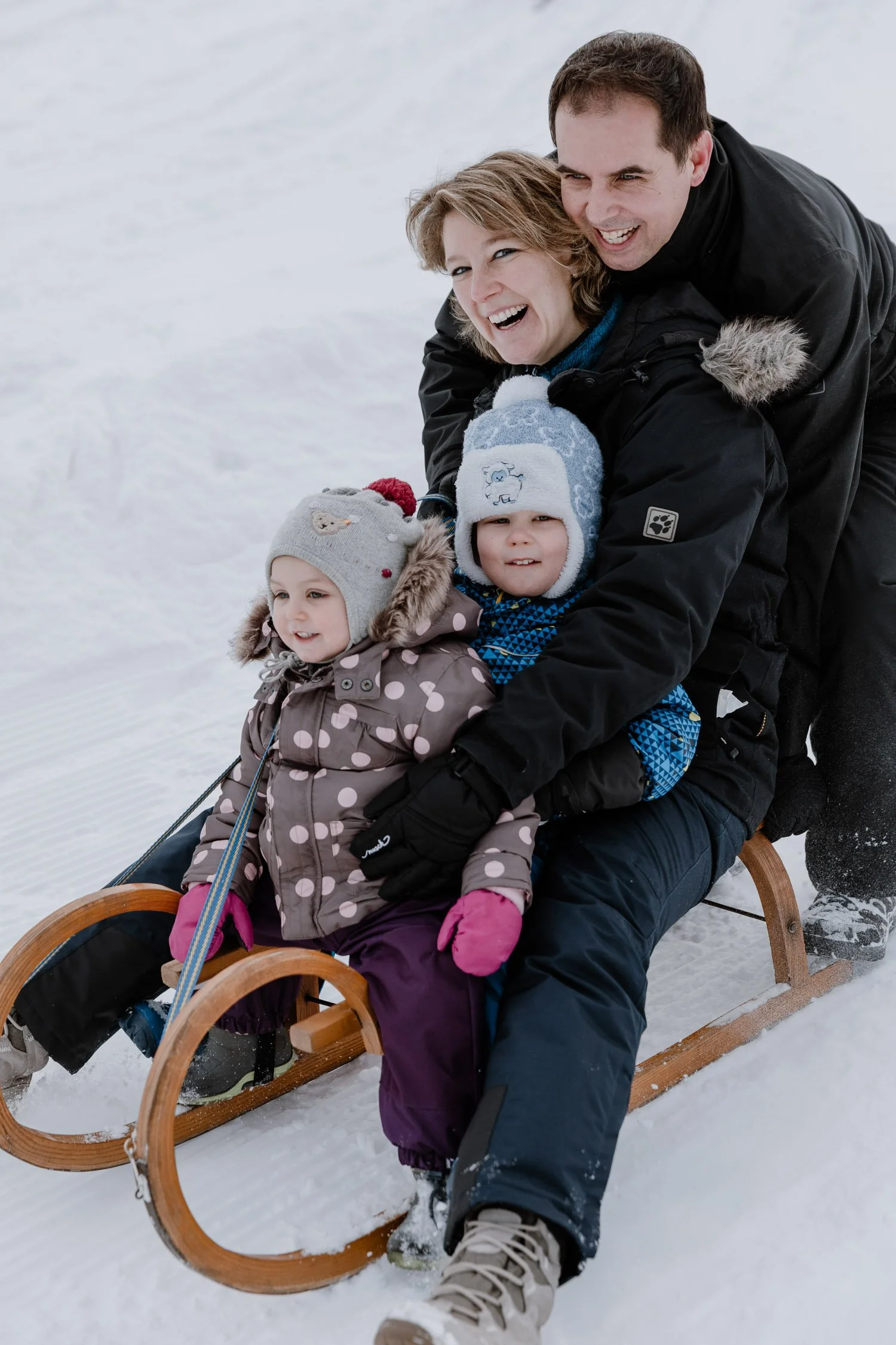 Familie beim Schlittenfahren im Schnee, lachend und fröhlich.