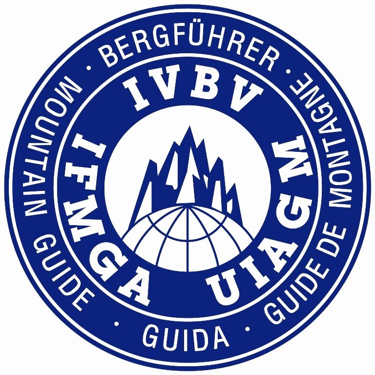 Ein runder Logo mit Berggipfeln, einer Weltkugel und italienischer und englischer Beschriftung.