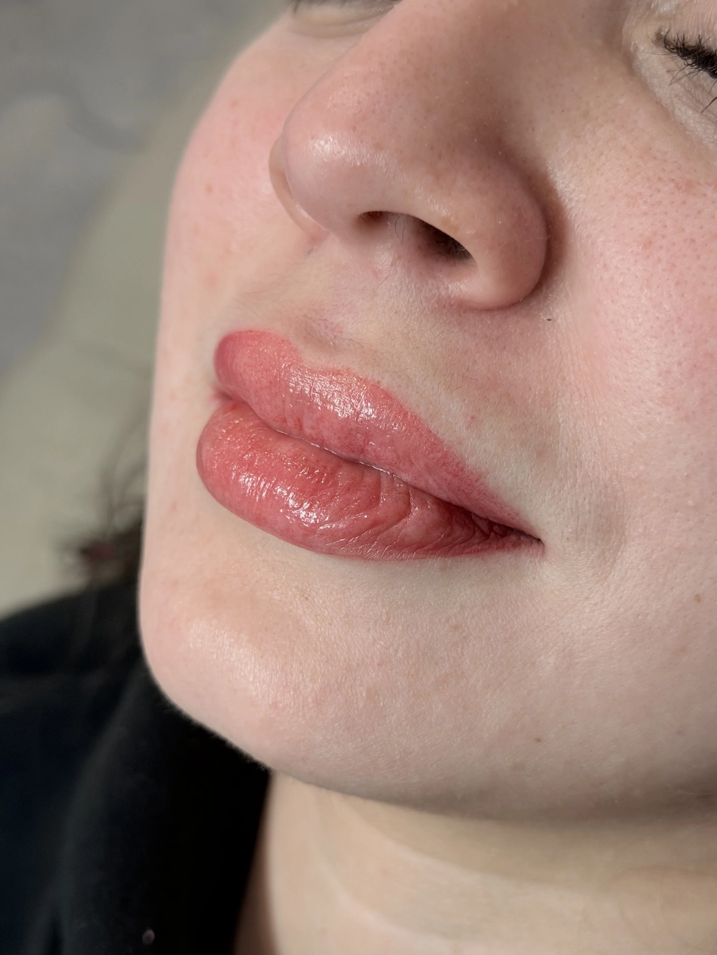 Close-up of a person's face showing the nose, lips, and part of an eye with makeup, with light skin and subtle freckles.